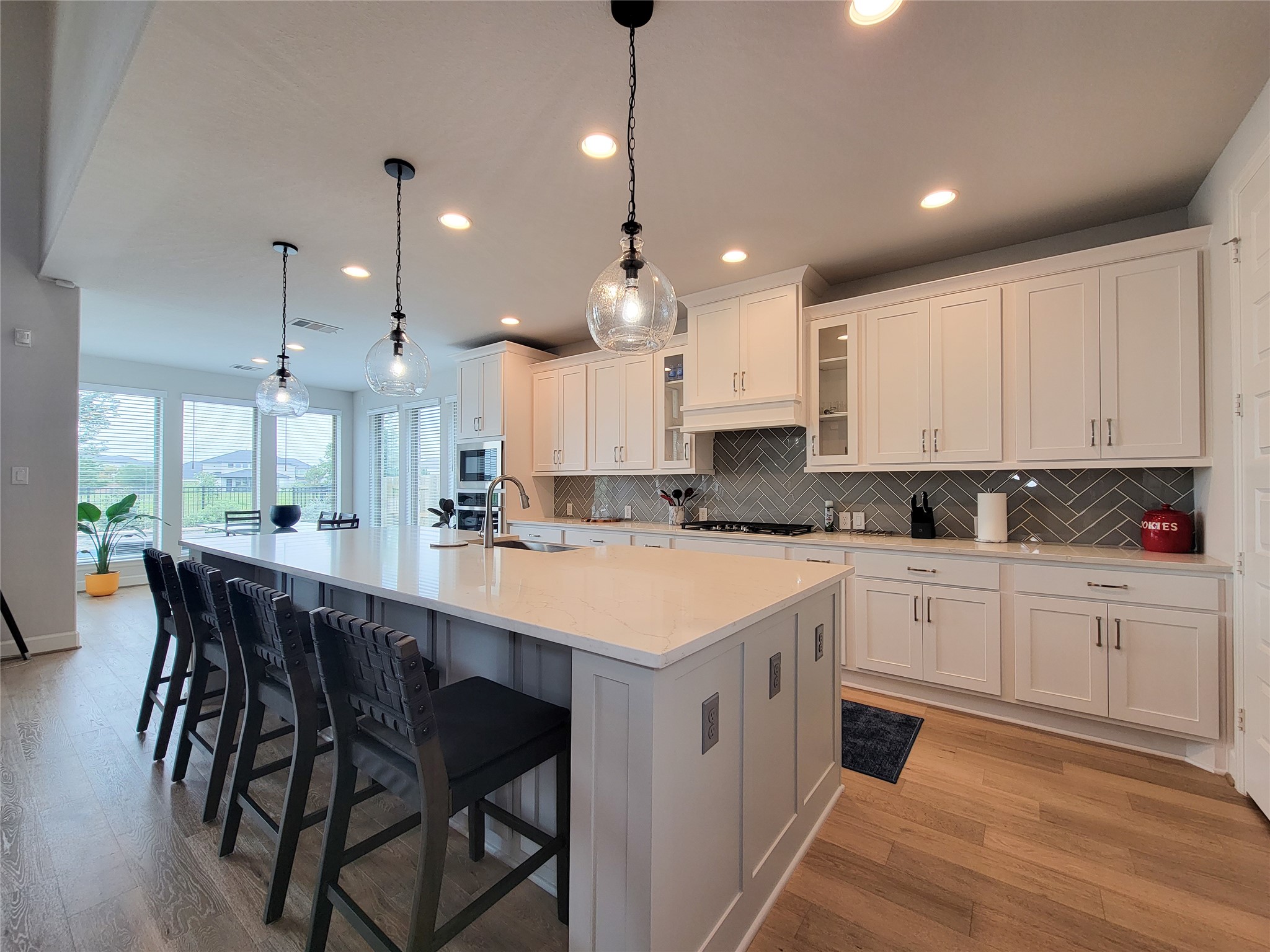 This modern kitchen boasts a spacious layout with a large island featuring seating for four. It includes sleek white cabinetry, stainless steel appliances, and stylish pendant lighting, all enhanced by ample natural light from the adjoining dining area. This modern kitchen boasts a spacious layout with a large island featuring seating for four. It includes sleek white cabinetry, stainless steel appliances, and stylish pendant lighting, all enhanced by ample natural light from the adjoining dining area.
