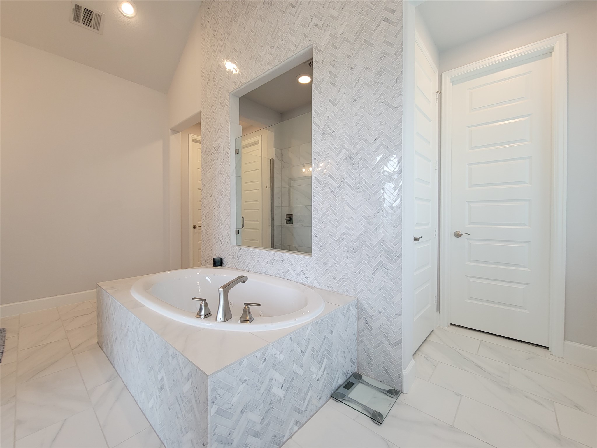 Modern bathroom with a large built-in bathtub, surrounded by elegant herringbone tile. The room is bright and spacious, with a neutral color palette and sleek fixtures.