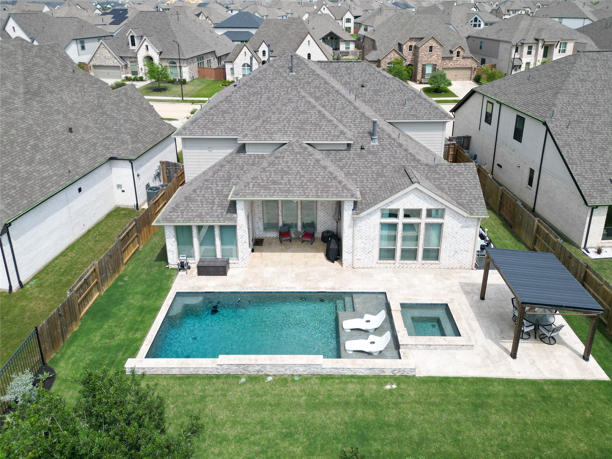 This aerial view showcases a modern home with a spacious backyard featuring a pool and spa. The property includes a covered patio area and is surrounded by a well-maintained lawn and privacy fences, set in a neighborhood with similar style homes. This aerial view showcases a modern home with a spacious backyard featuring a pool and spa. The property includes a covered patio area and is surrounded by a well-maintained lawn and privacy fences, set in a neighborhood with similar style homes.