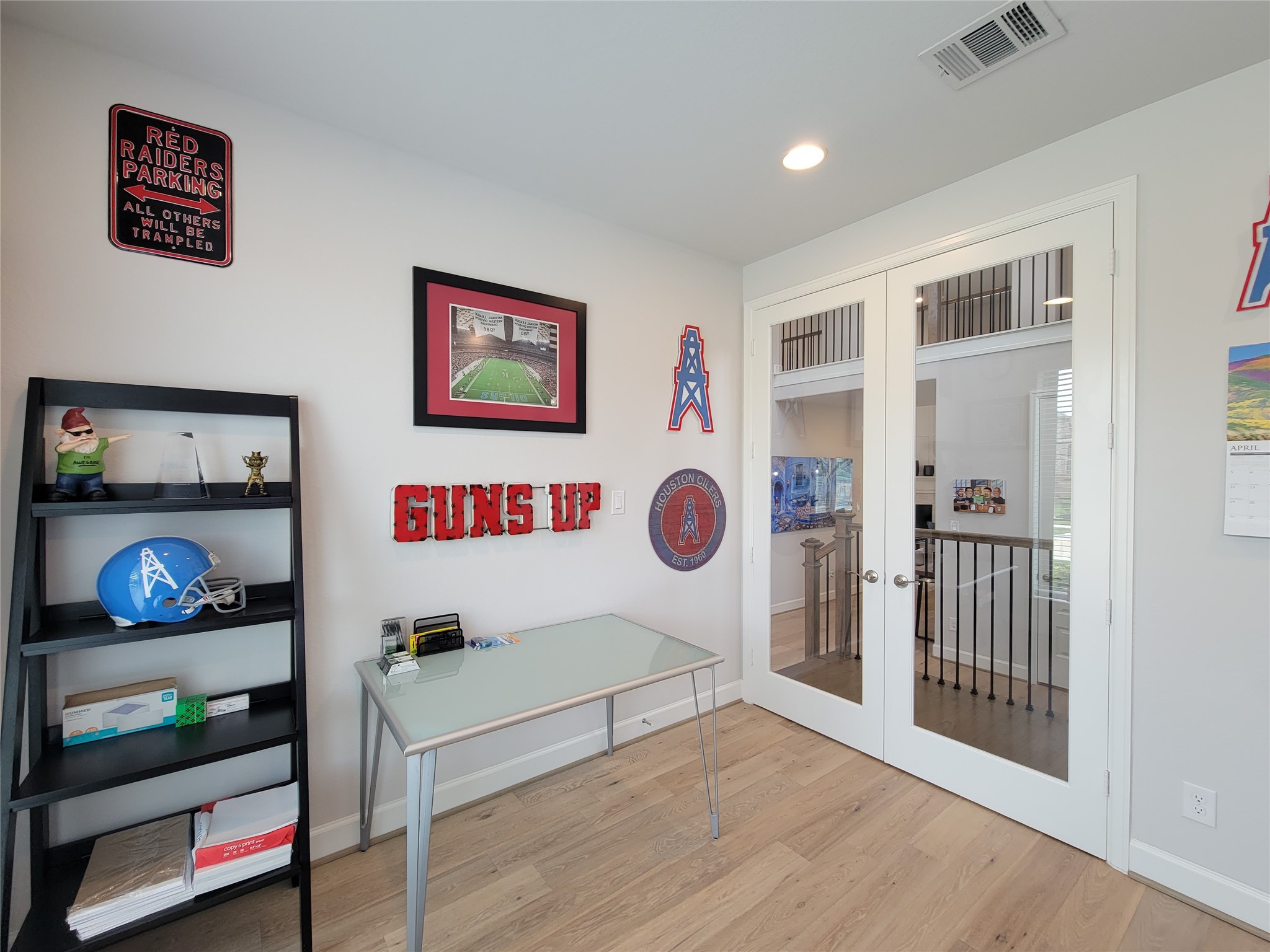 Bright home office with glass double doors, light wood flooring, a modern desk, and a shelving unit.
