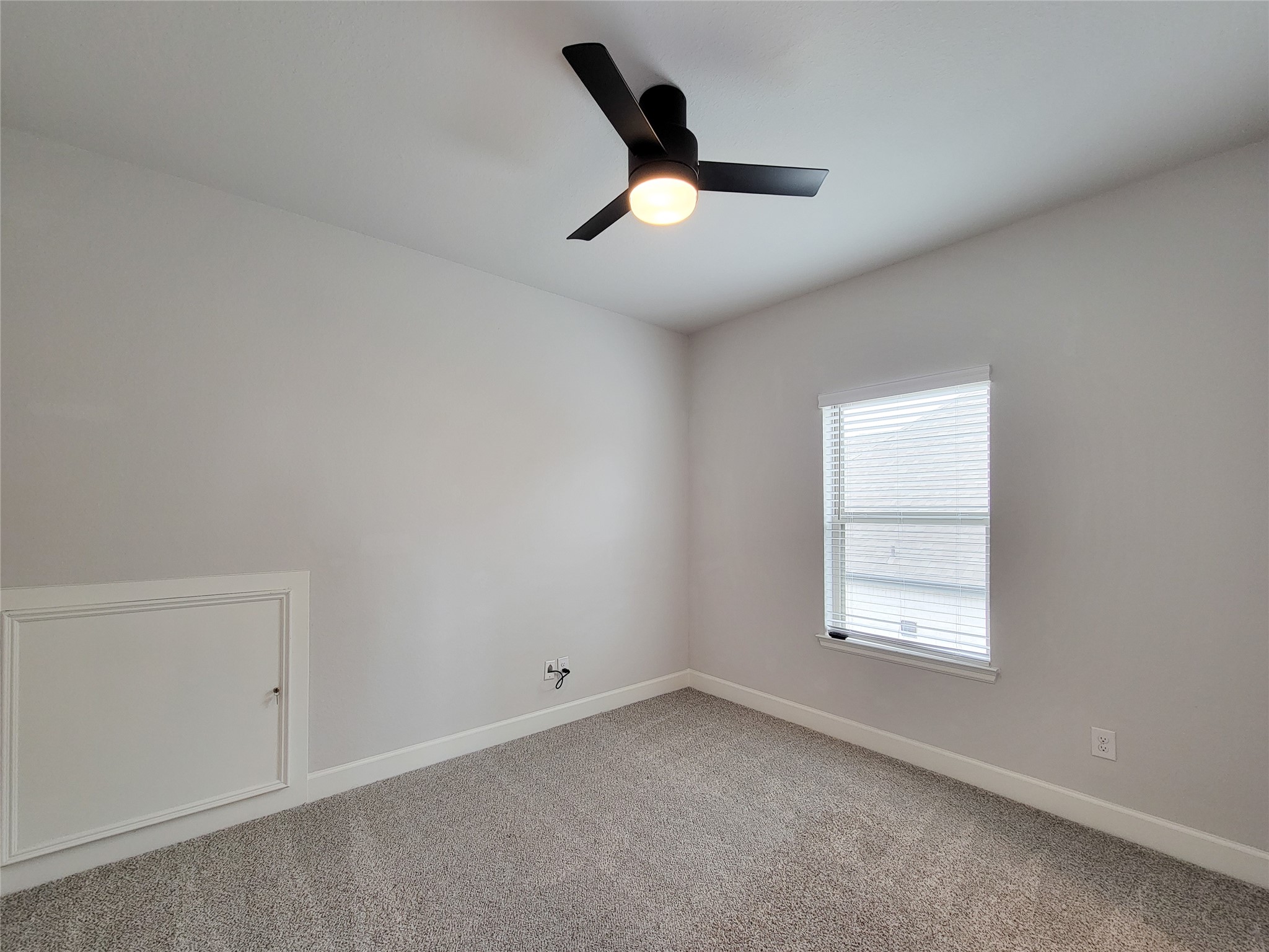 This Bedroom shows a bright, small room with neutral-color walls and carpet. It features a modern ceiling fan and a window with blinds, providing natural light.