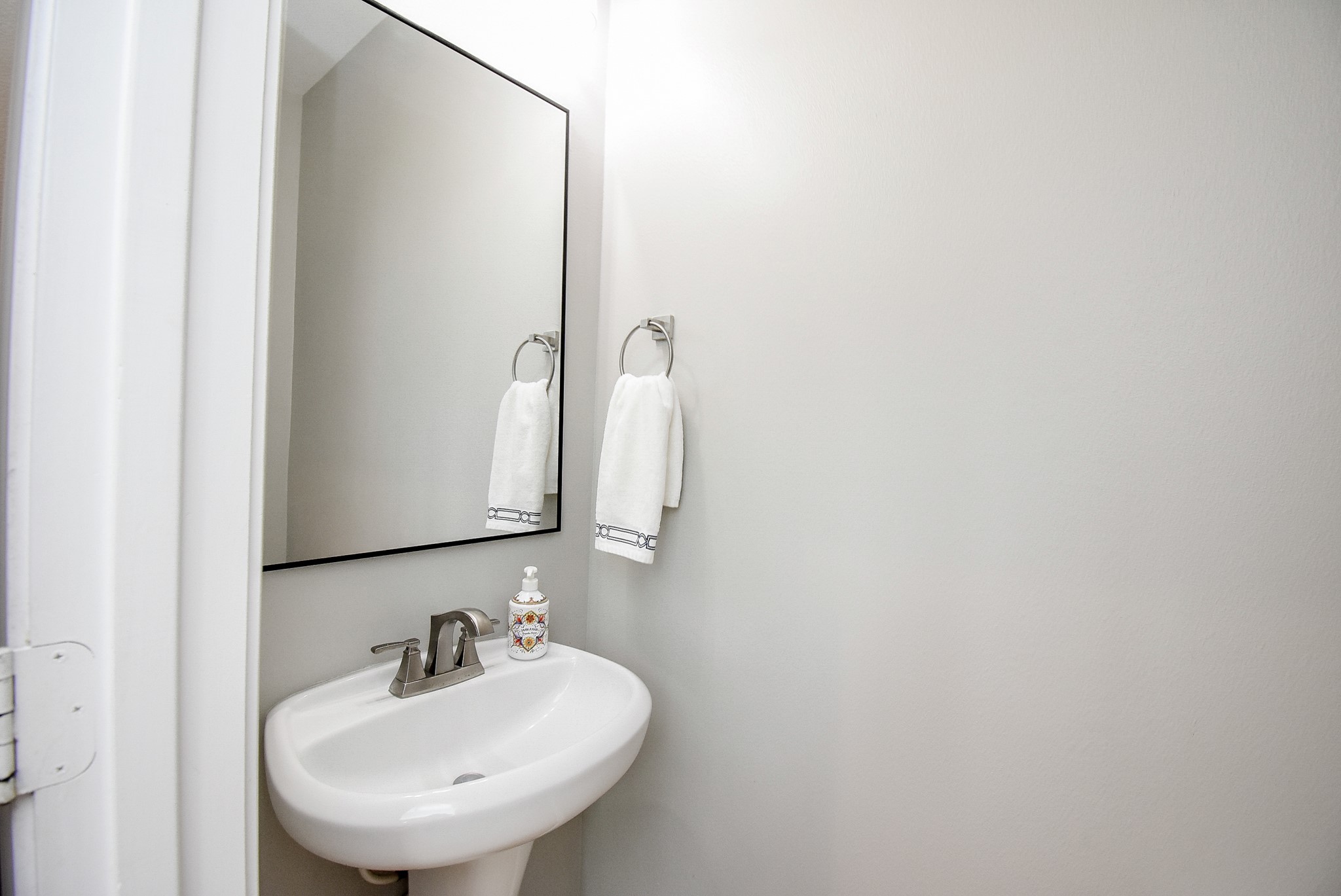 Updated guest half bath with modern pedestal sink, black from mirror, updated vanity lights and fresh paint.