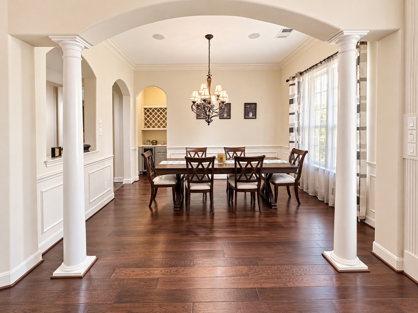 Beautiful formal dining room with crown molding, elegant chandelier, and classic wainscoting.arched openings, and an inviting view into the home.