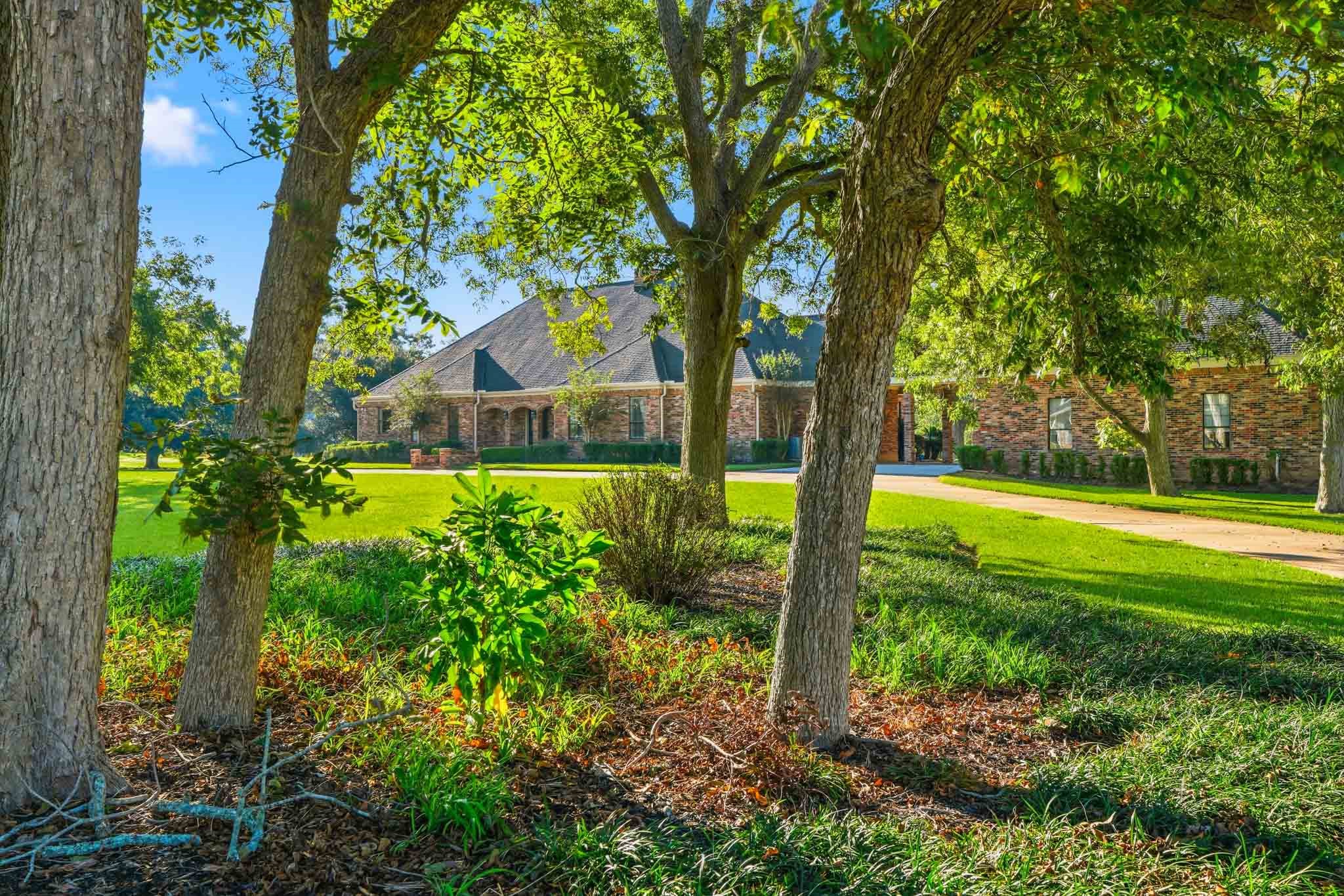 Stunning brick home set amidst lush greenery, offering serene views and ample privacy with mature trees and a well-maintained lawn.