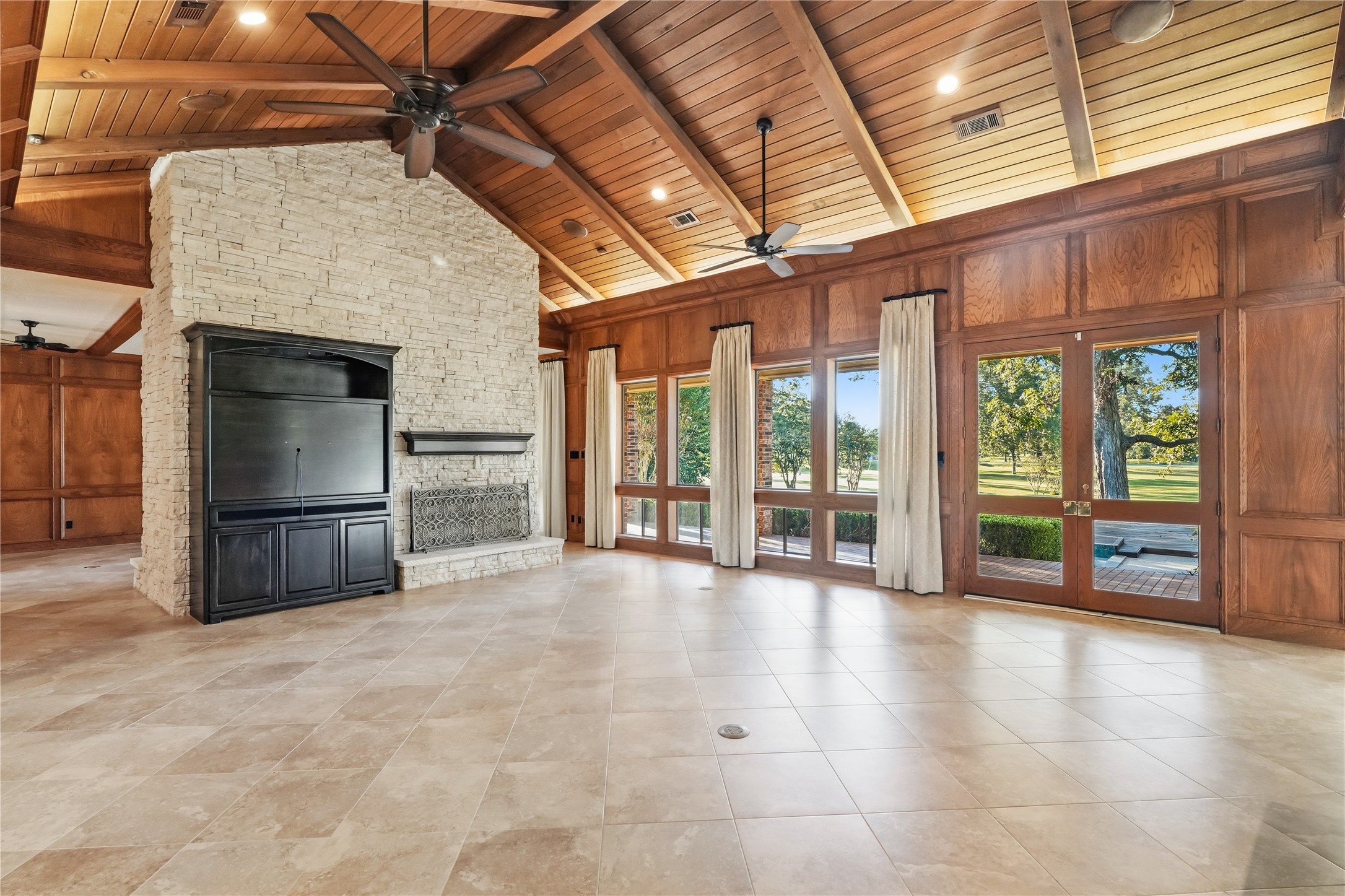 Spacious living area with a stunning vaulted wood ceiling, stone fireplace, and large windows offering beautiful views, perfect for entertaining or relaxing.