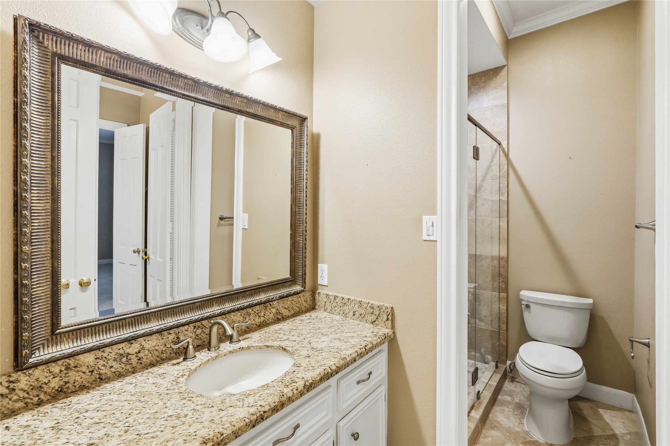 Bathroom featuring a granite countertop, a large framed mirror, and a glass-enclosed shower, offering both style and functionality.