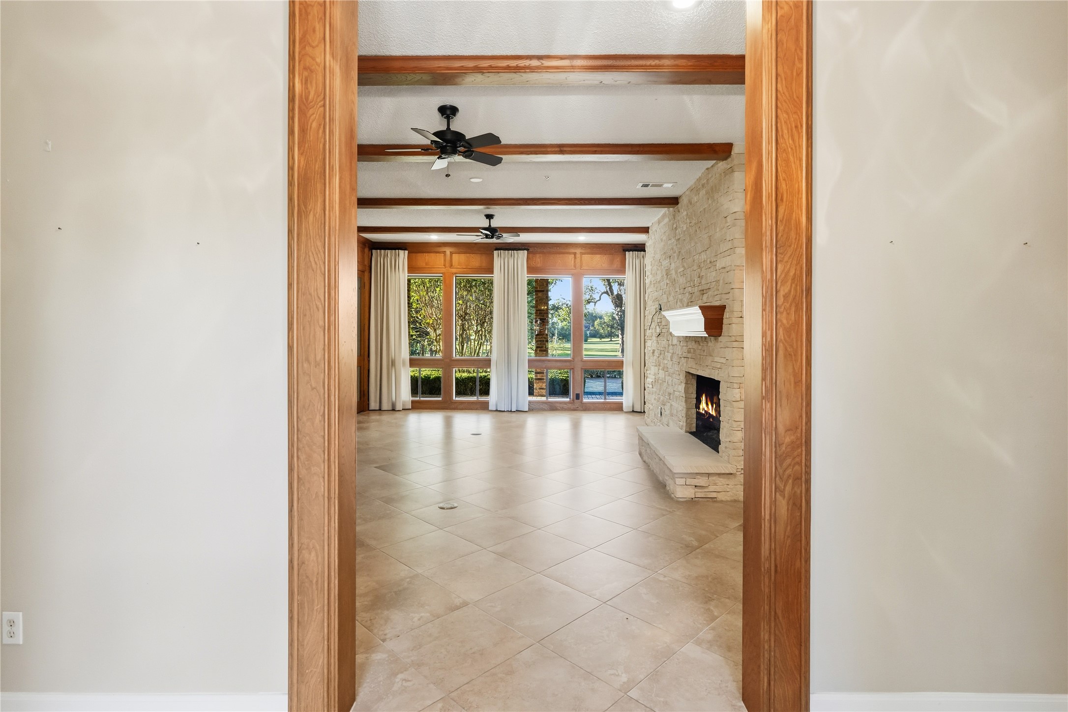 Elegant living room with a cozy stone fireplace, large windows offering scenic views, and rich wood beam accents on the ceiling.
