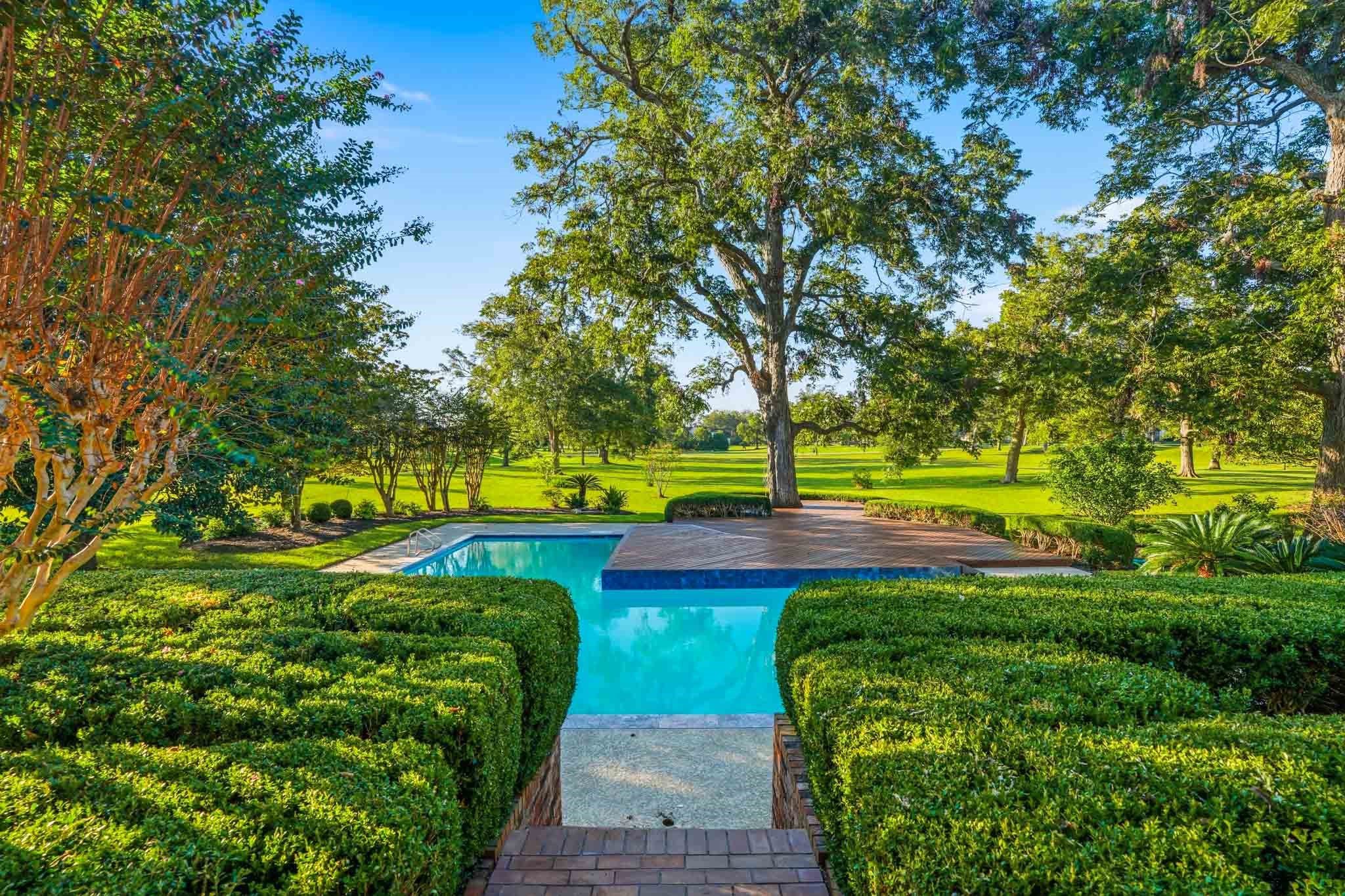 Luxurious poolside oasis with manicured hedges and mature trees, offering serene views of expansive green lawns.