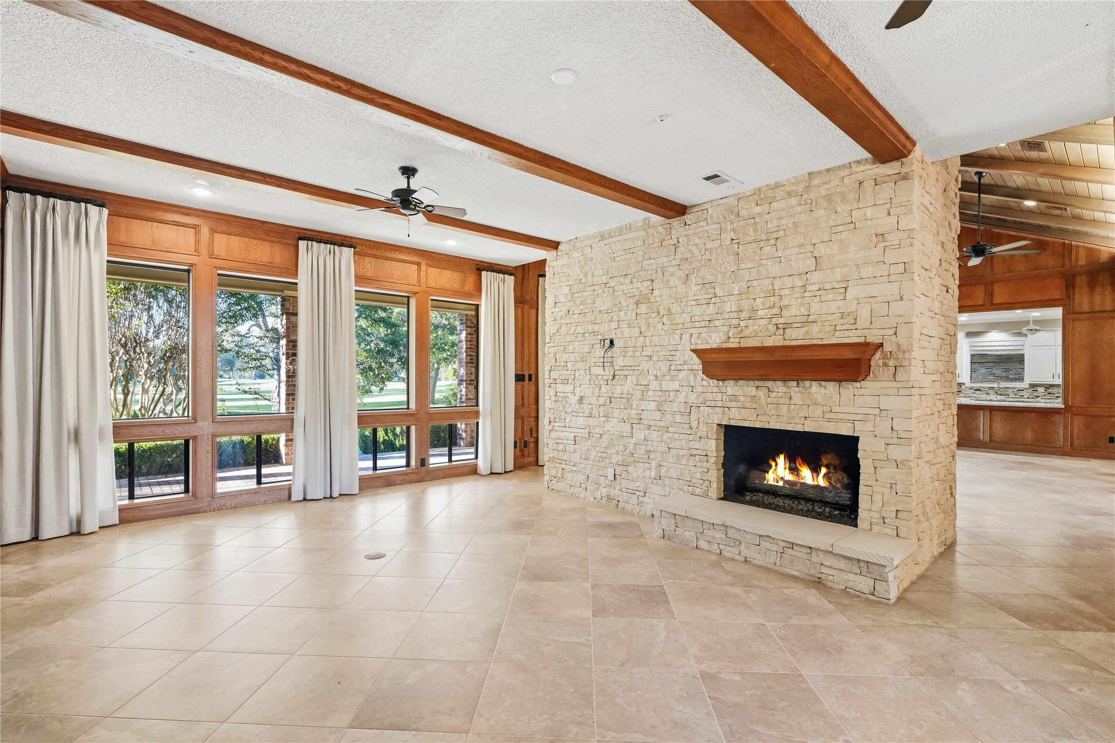 Spacious living area featuring a stunning stone fireplace, large windows with serene views, and elegant tile flooring.