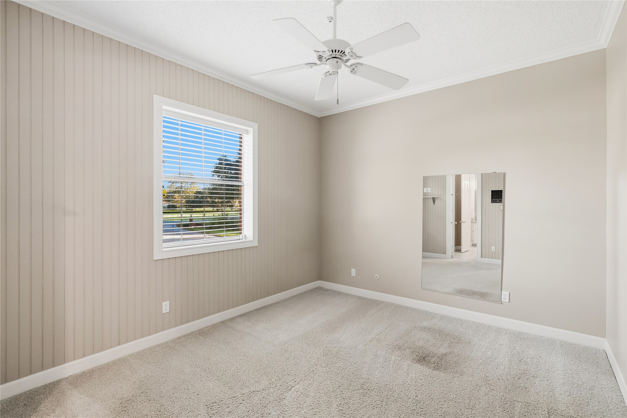 Bright room with neutral tones, featuring a large window with blinds, a ceiling fan connected to a bathroom.