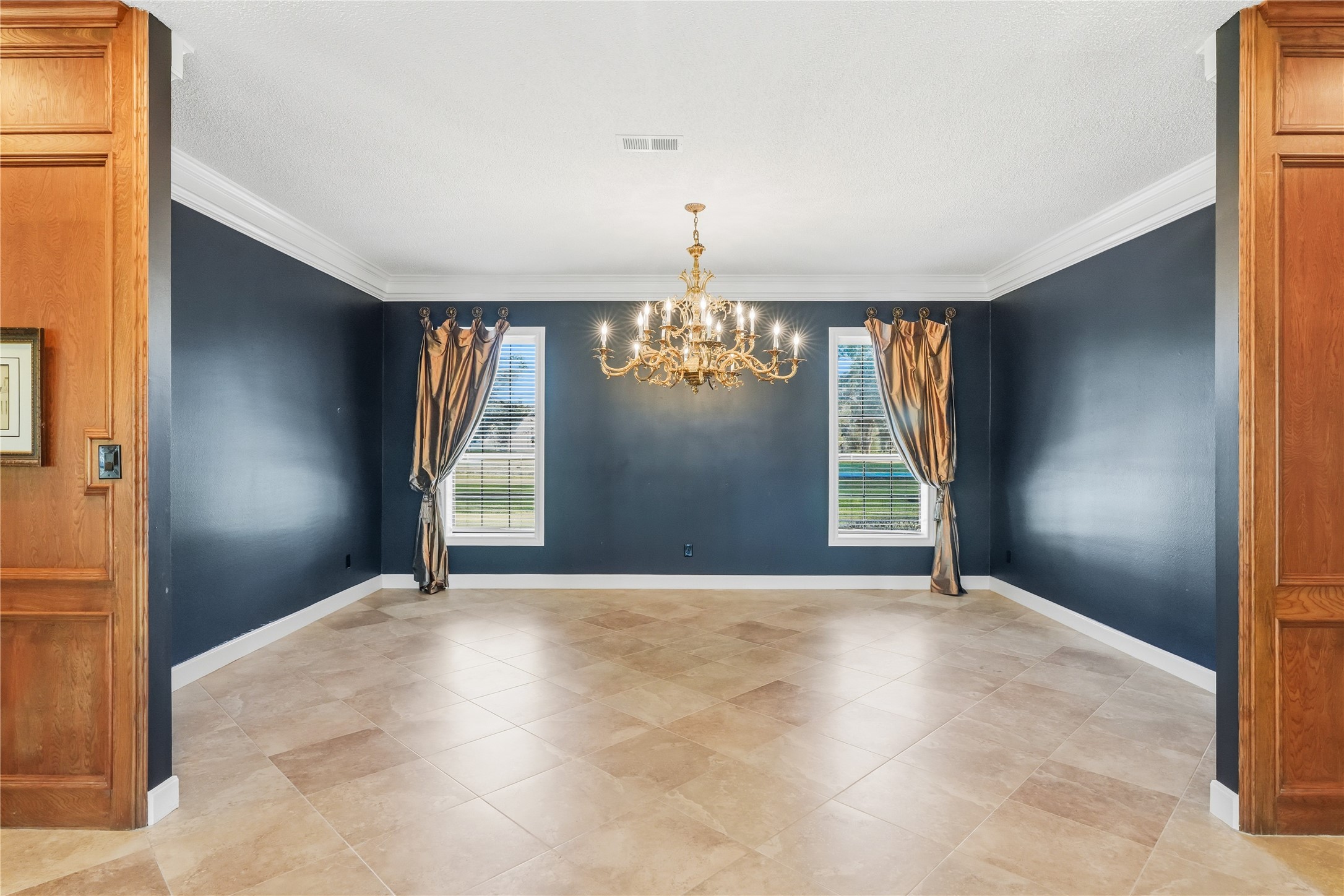 Dining room featuring a stunning chandelier, and large windows with drapes, complemented by warm tile flooring.