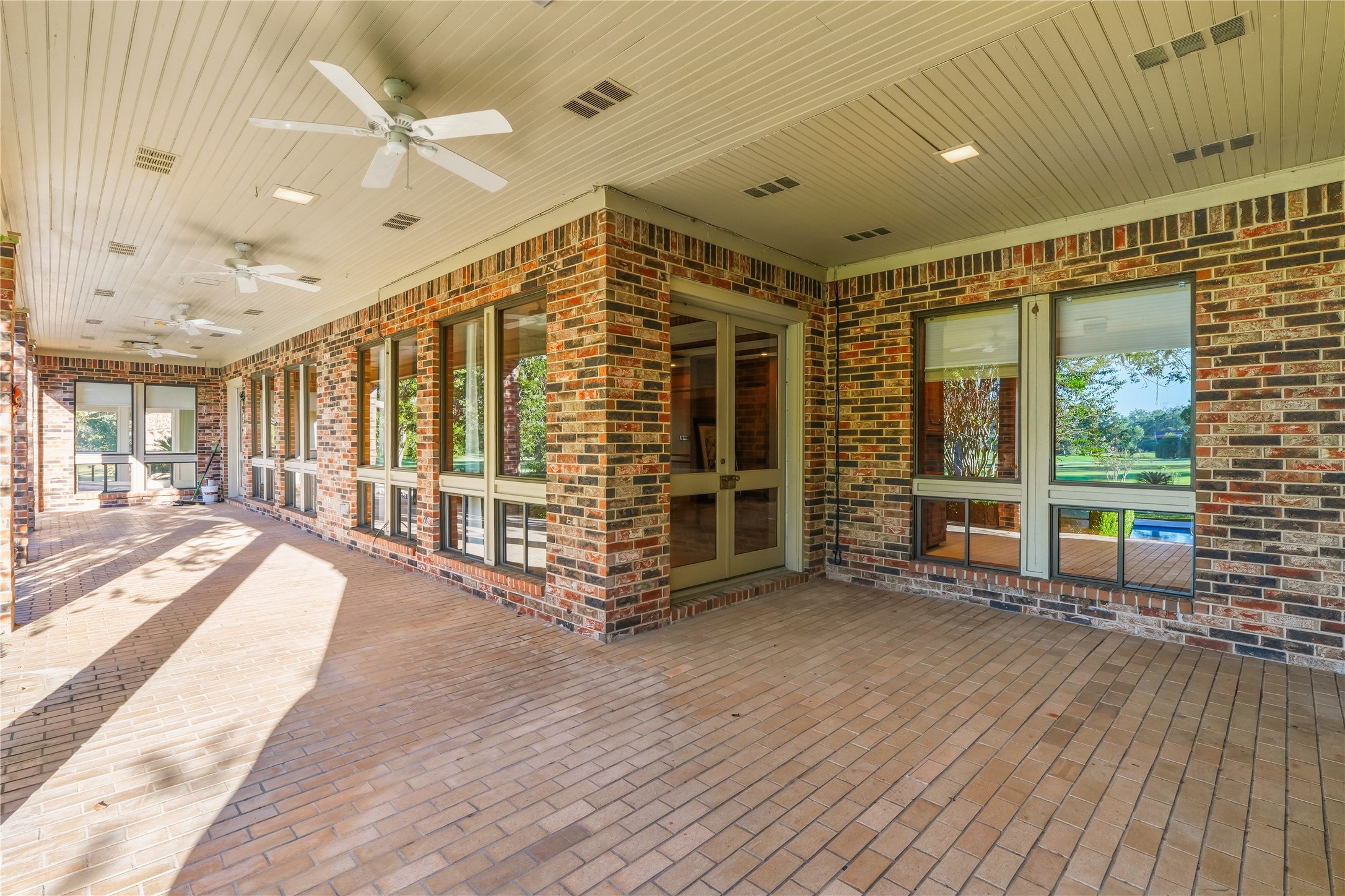 Expansive covered patio with brick flooring and ceiling fans, offering a perfect space for outdoor relaxation and entertaining.