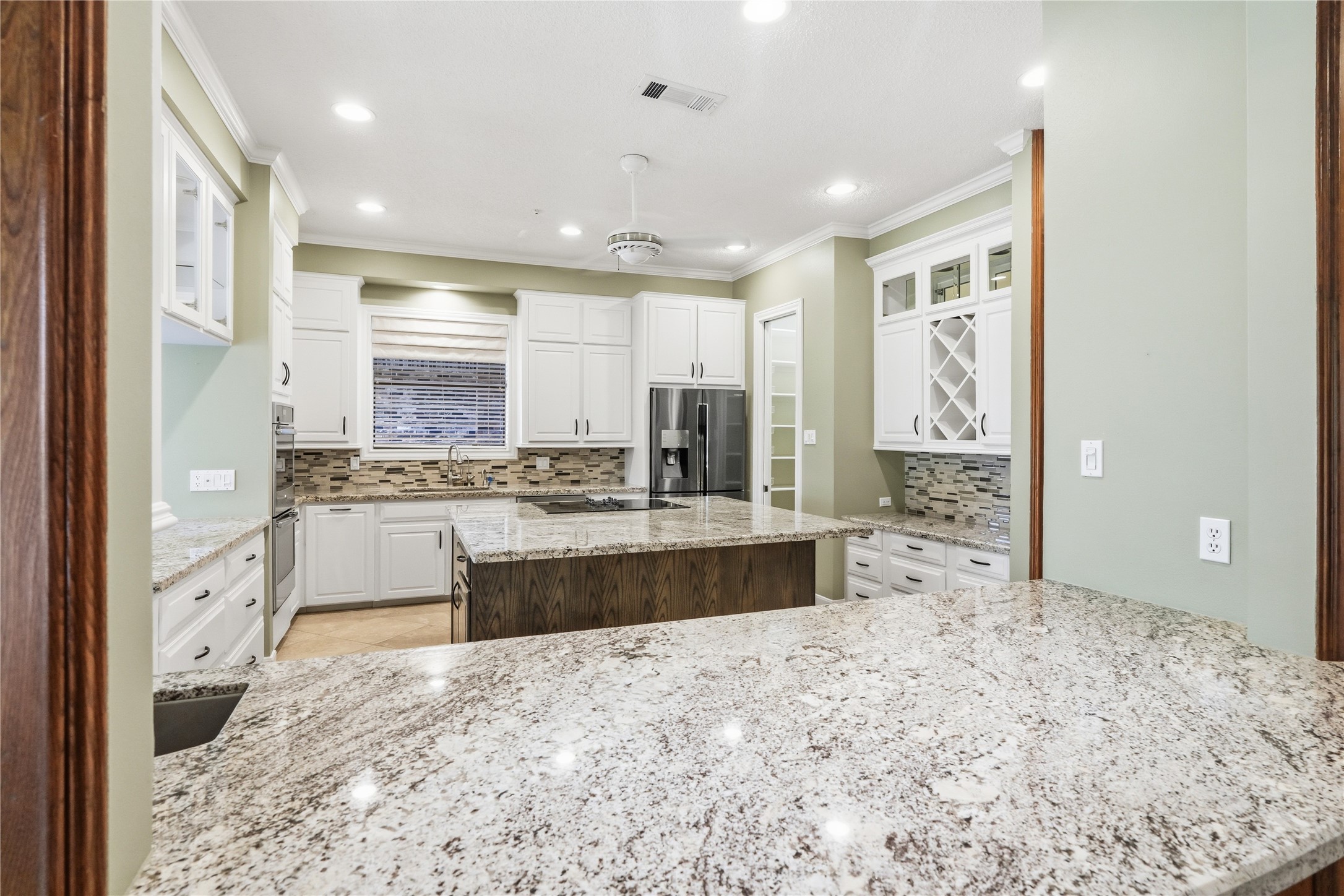 Spacious kitchen with granite countertops, white cabinetry, a central island, and modern stainless steel appliances, perfect for culinary enthusiasts.