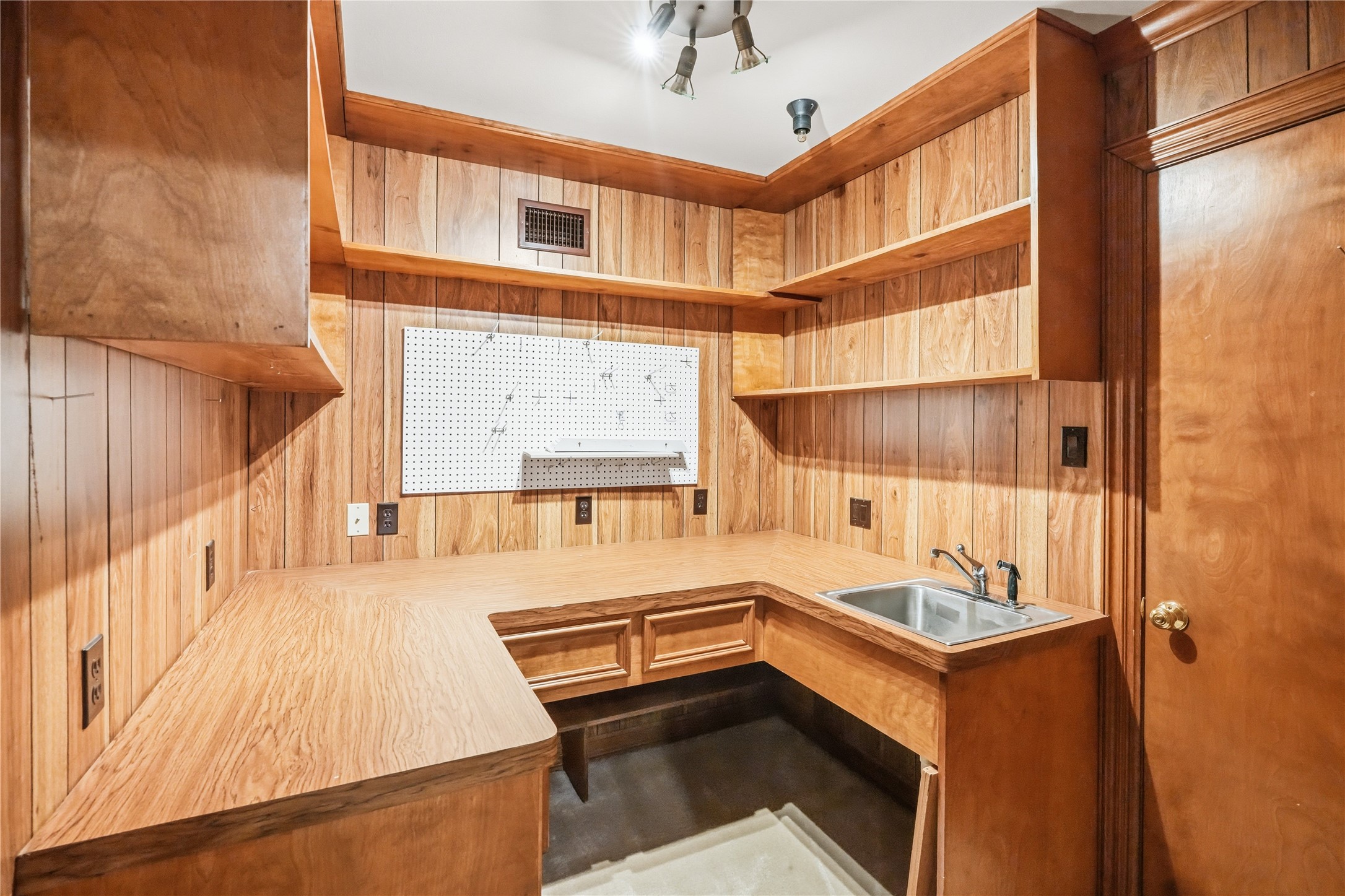 Cozy workshop space with warm wood paneling, ample shelving for storage, and a convenient utility sink for versatile use.