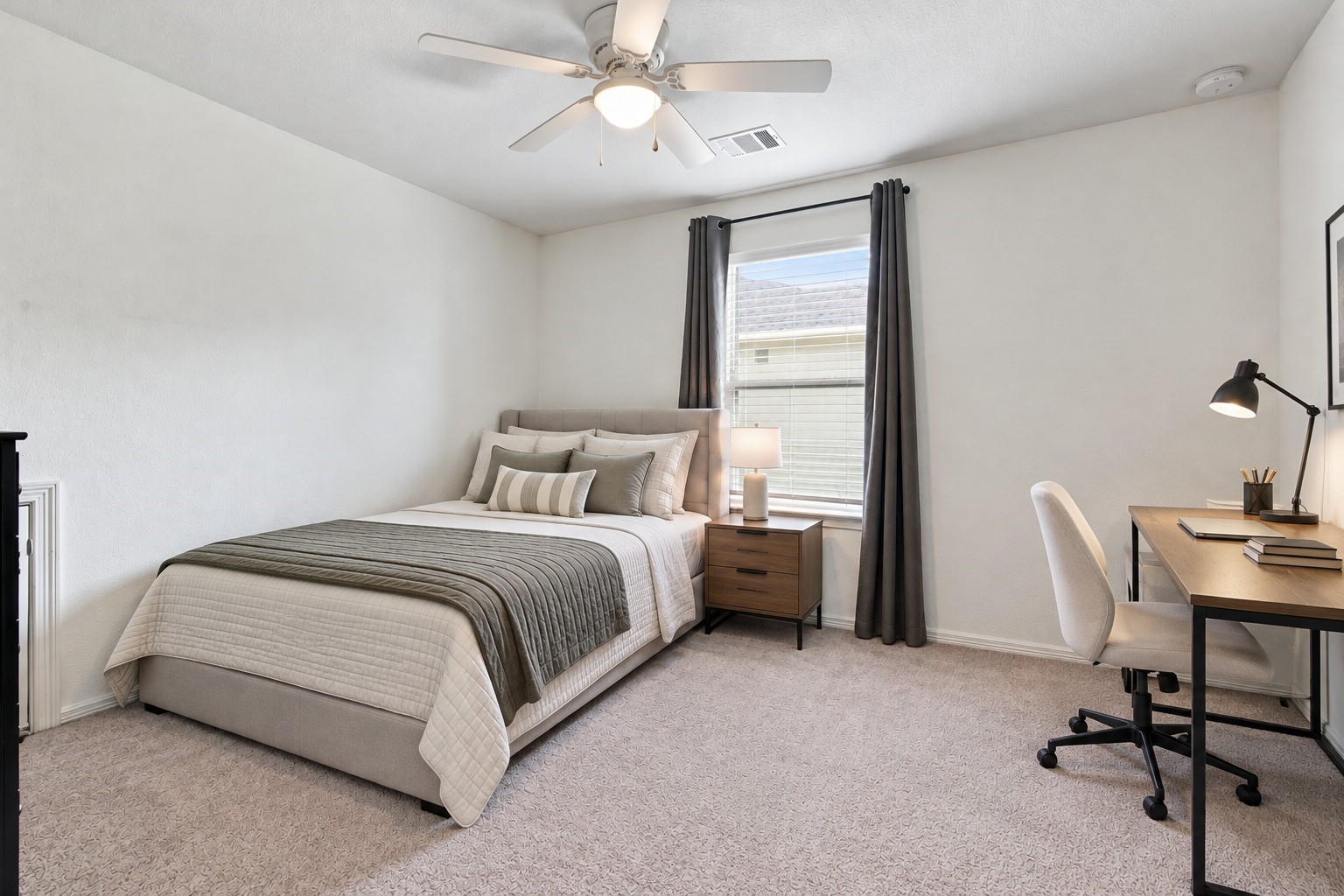 Virtually Staged: This secondary bedroom offers a bright, spacious layout with a modern design and soothing neutral tones. Crisp white walls, soft carpeting, and a large window with elegant gray curtains and white blinds create an airy atmosphere filled with natural light. A dedicated workspace area provides an ideal setting for studying or working from home.