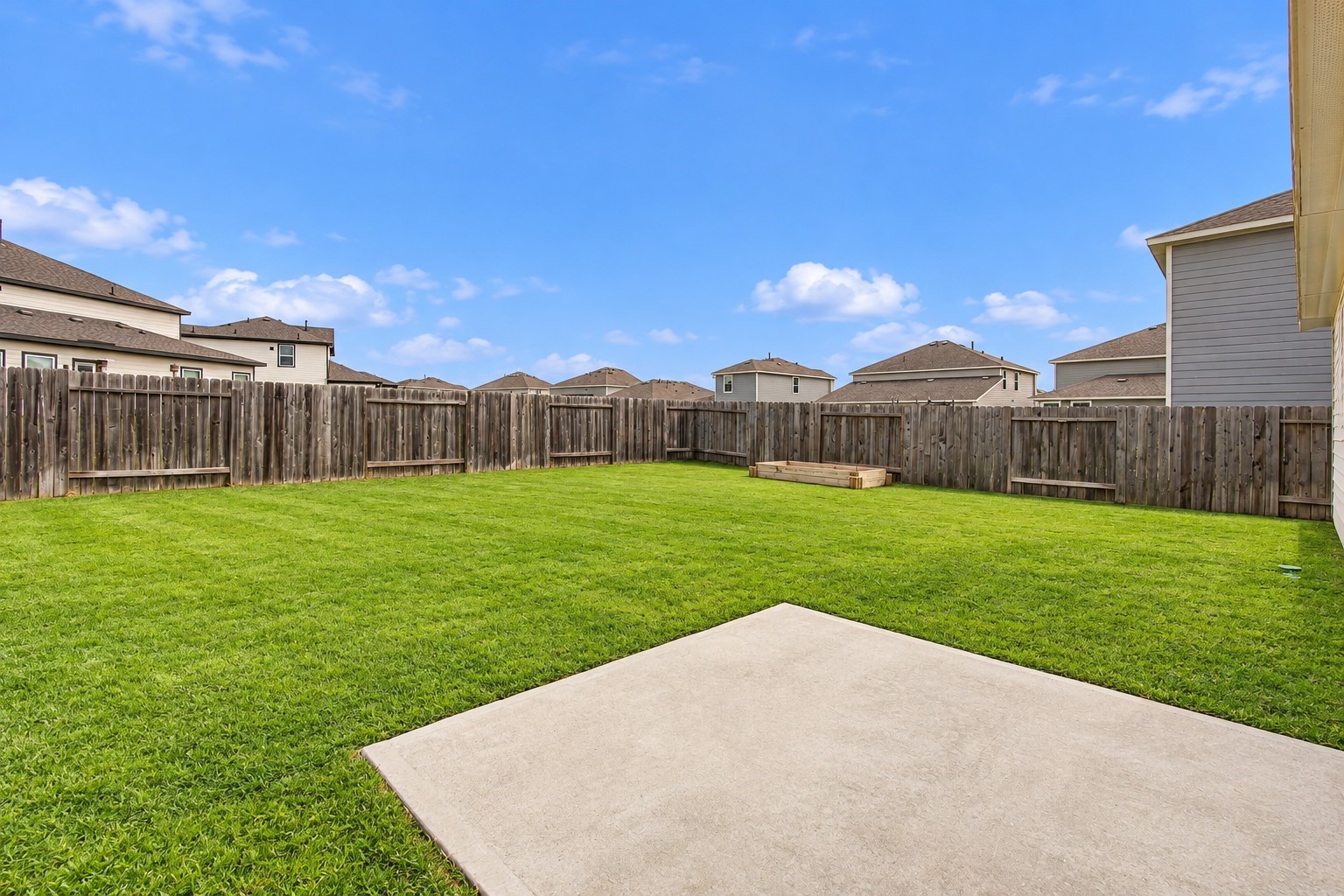A generously sized concrete patio provides an ideal setting for outdoor seating, grilling, or dining. The expansive grassy area offers endless possibilities for outdoor activities, or creating a personalized backyard retreat.