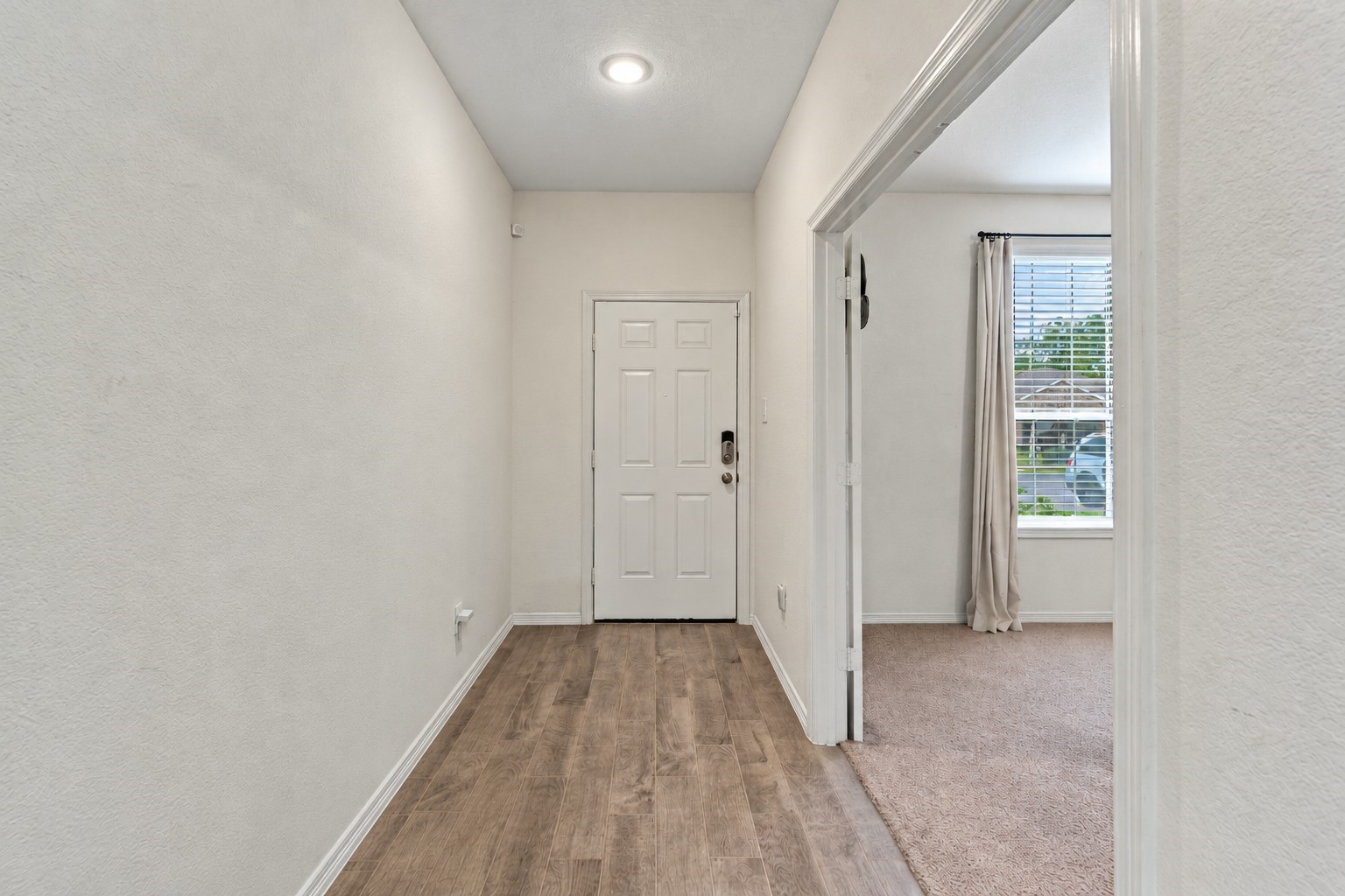 This bright and welcoming entryway features a clean, modern design with soft neutral walls, rich wood-look flooring, and crisp white baseboards.