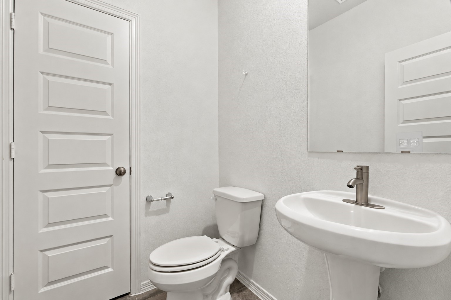 This charming half bath features a clean, modern design with crisp white textured walls and stylish wood-look tile flooring.