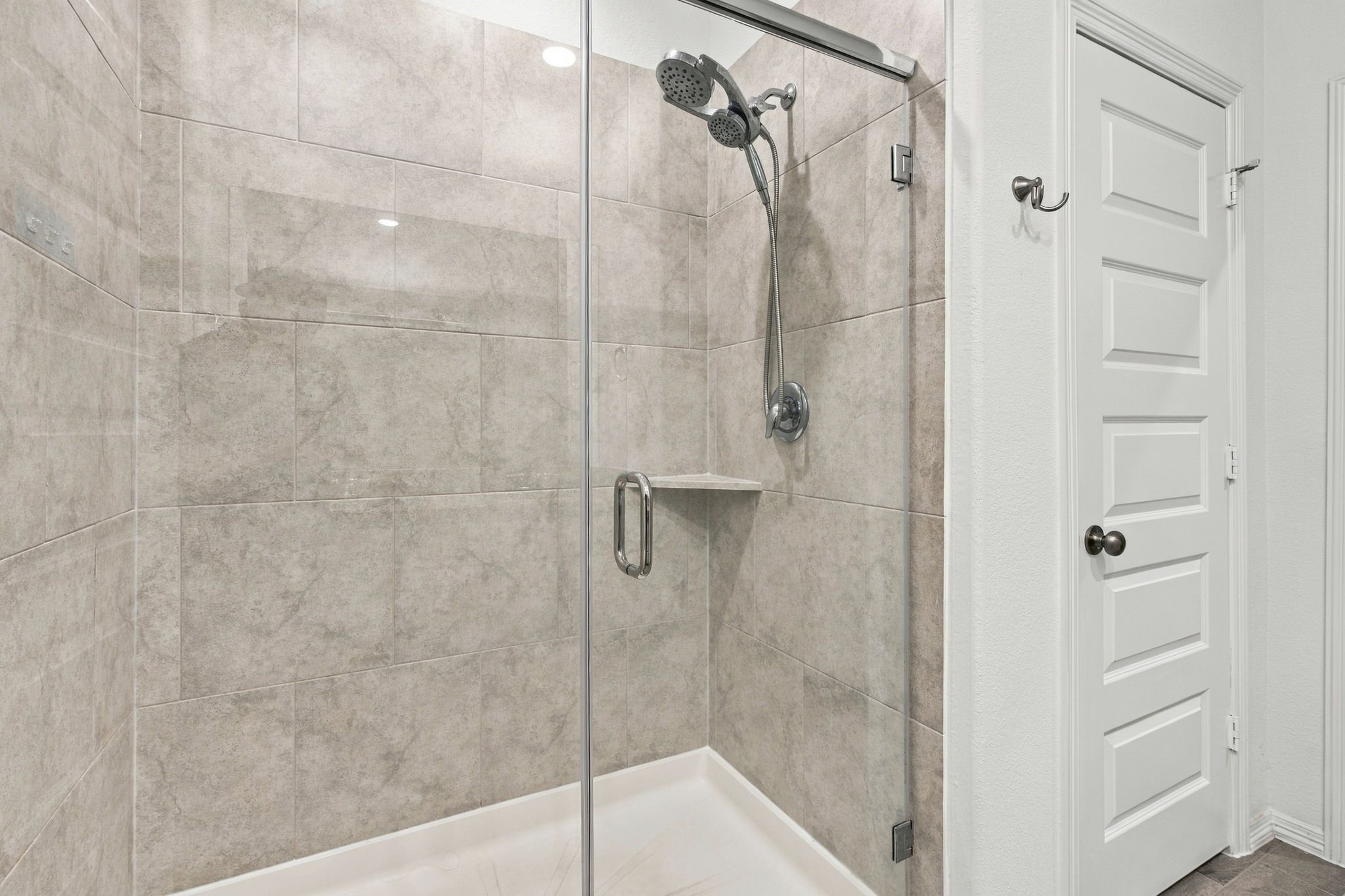 This beautifully designed walk-in shower features elegant, large-format gray tile extending from floor to ceiling, creating a sleek and modern appearance. A frameless glass enclosure with a chrome handle adds a sophisticated touch while maintaining an open, airy feel.