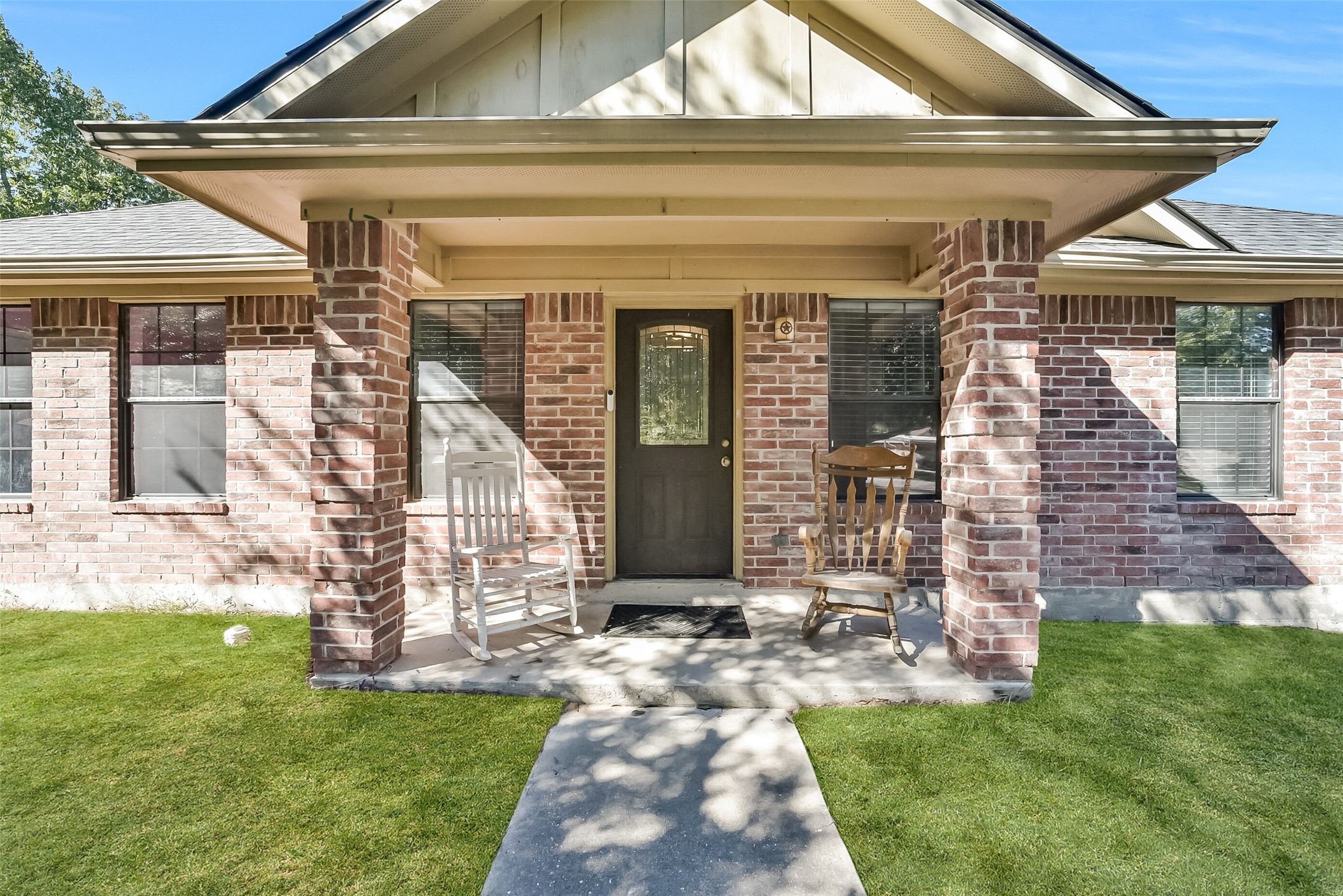 This charming one-story home showcases a classic brick elevation with a welcoming covered front porch framed by substantial brick columns. A decorative glass front door adds character, while the shaded porch offers an inviting spot to relax and enjoy your morning coffee.