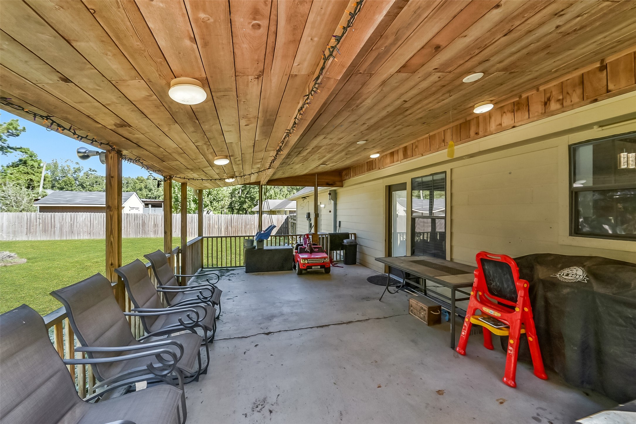 Enjoy outdoor living on this spacious covered patio, featuring a wood-plank ceiling, overhead lighting, and views of the large fenced backyard. With ample room for dining, relaxing, and entertaining, this inviting space offers a shaded retreat just steps from the home.
