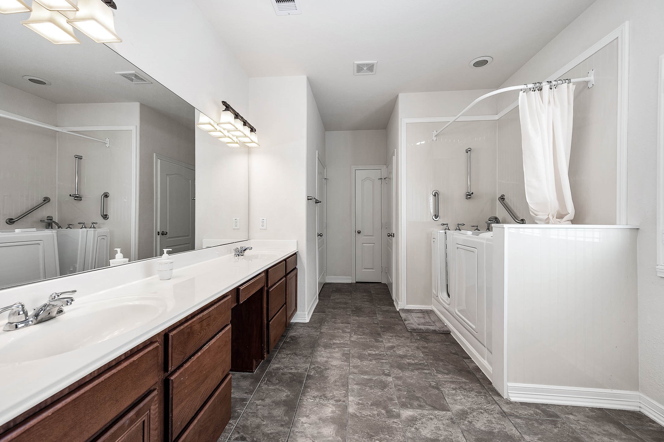 Experience the luxurious primary bedroom featuring double sinks, a stylish vanity area, and a handicap accessible tub/shower for ultimate comfort and convenience.