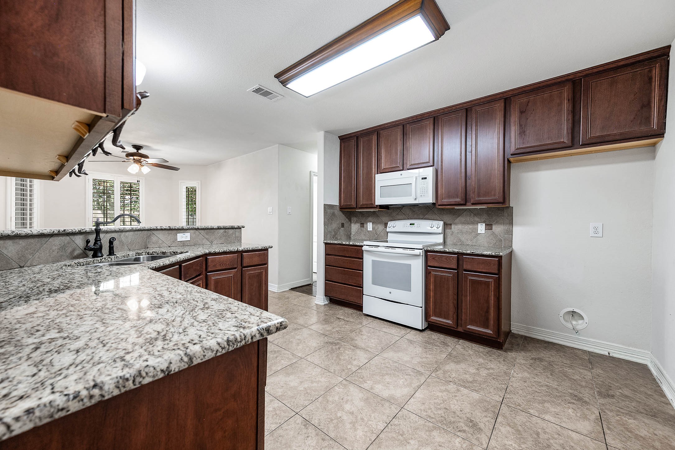 Experience culinary delight in this spacious kitchen with elegant countertops, rich cabinetry, and a generous spot ready for your dream refrigerator.