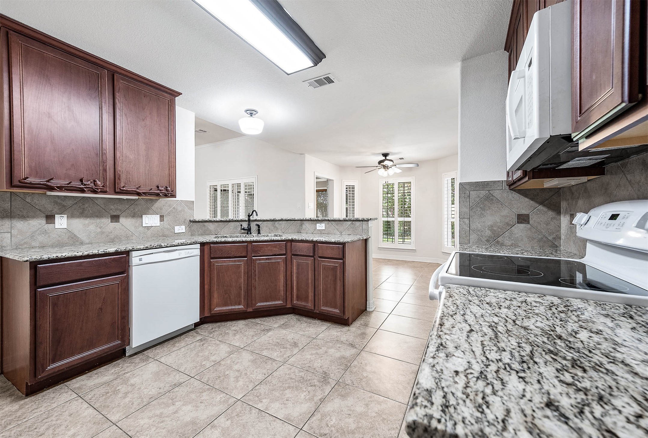Discover the heart of this home with a spacious kitchen featuring an electric range, dishwasher, and microwave, all set against elegant granite countertops and rich wood cabinetry.