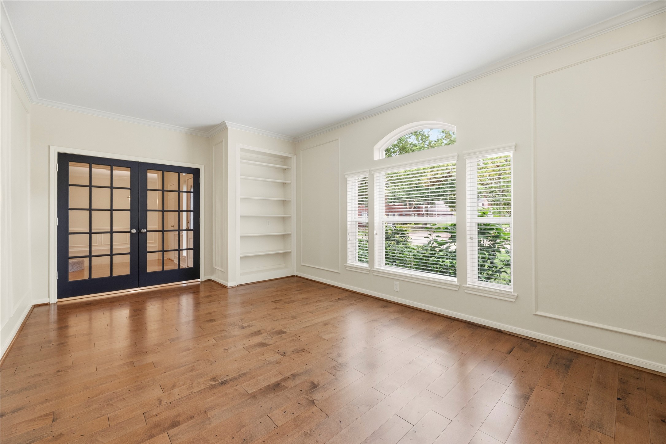 Elegant, dedicated study/office featuring engineered wood floors, large windows, built-in shelving, and stylish French doors.