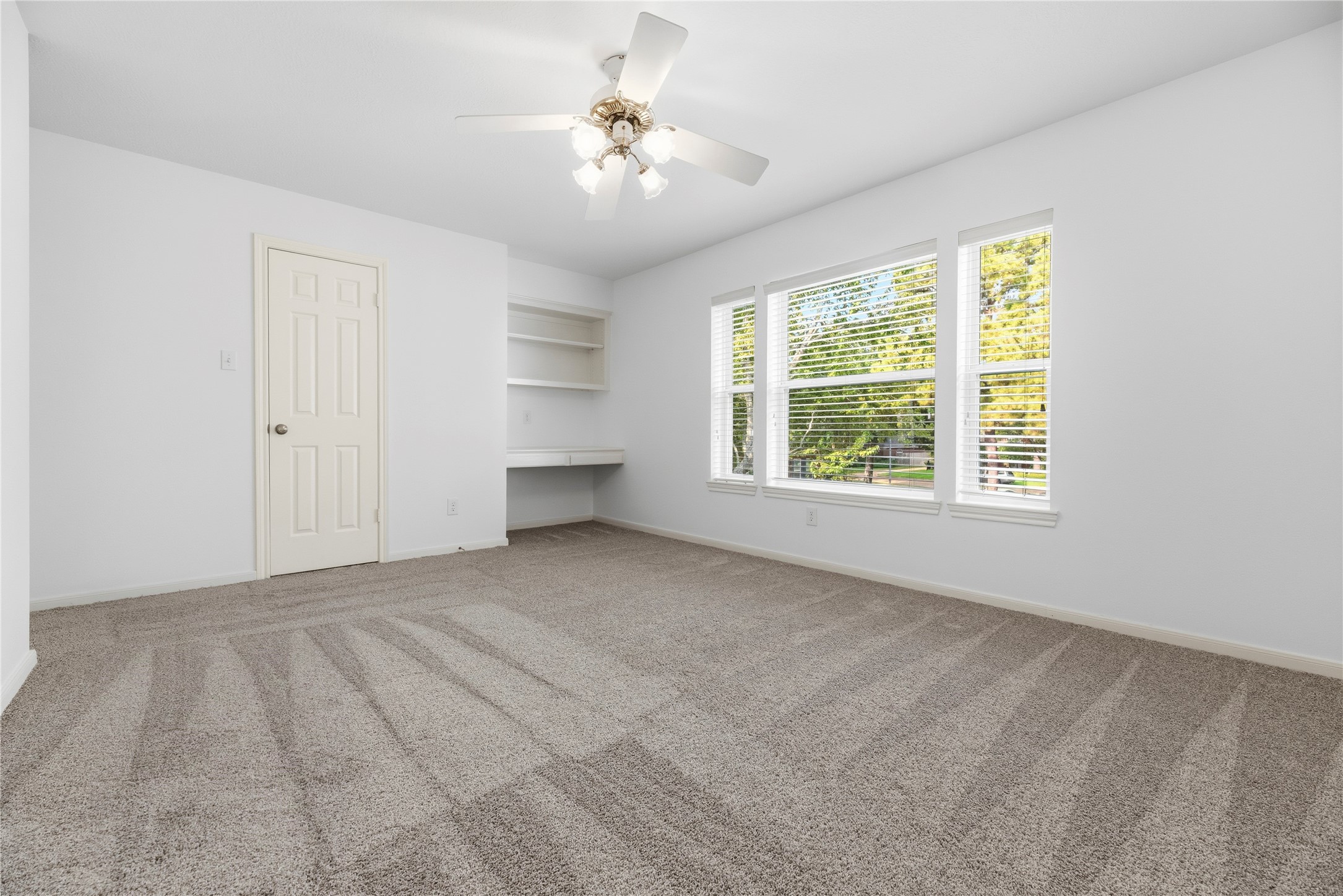 Bright secondary bedroom with plush carpeting (upgraded pad and carpet replaced in 2022). A built-in desk and shelving add functionality to the space.