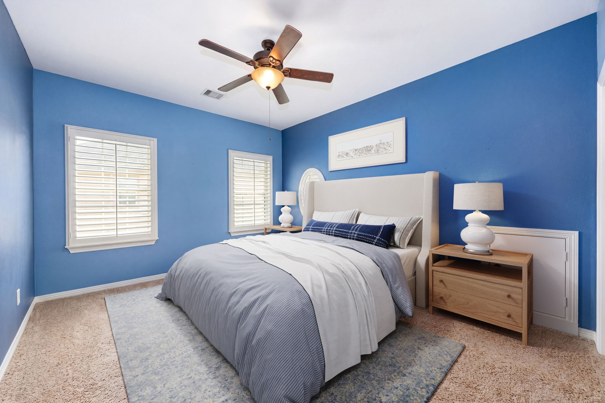 A bright and cheerful secondary bedroom featuring bold blue accent walls, plush carpet, plantation shutters, and a ceiling fan. The perfect space to personalize and make your own! *Virtually Staged