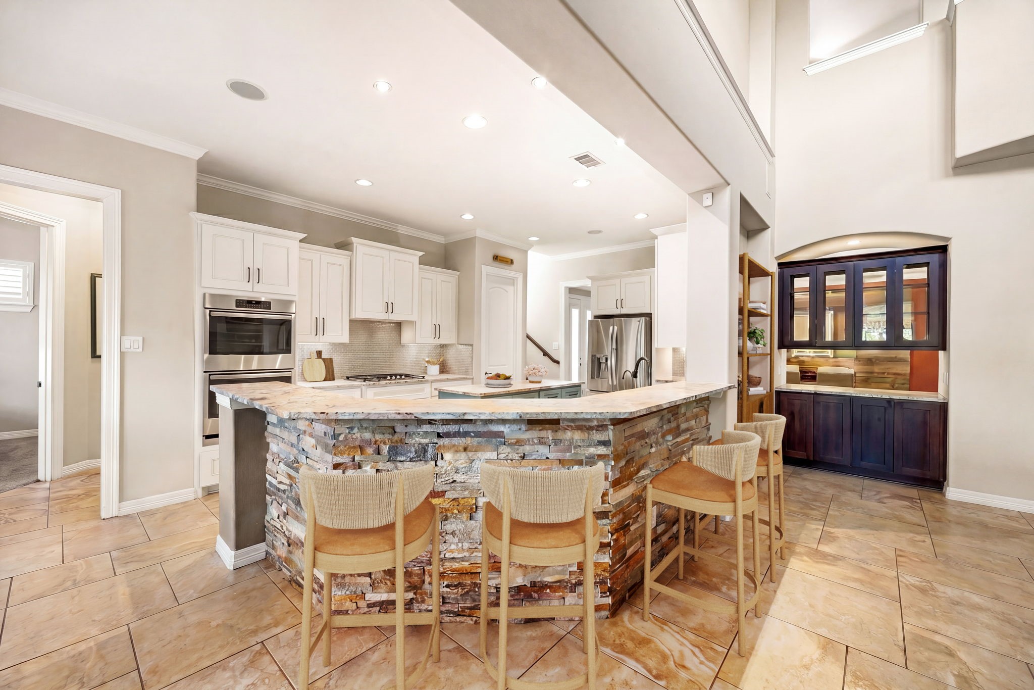 Now THIS is a showstopper! The dramatic stacked stone breakfast bar with granite countertops, built-in oven, stainless appliances, white cabinetry, and a stunning wet bar nook make this kitchen unlike anything else. Entertaining just got a serious upgrade. *Virtually Staged