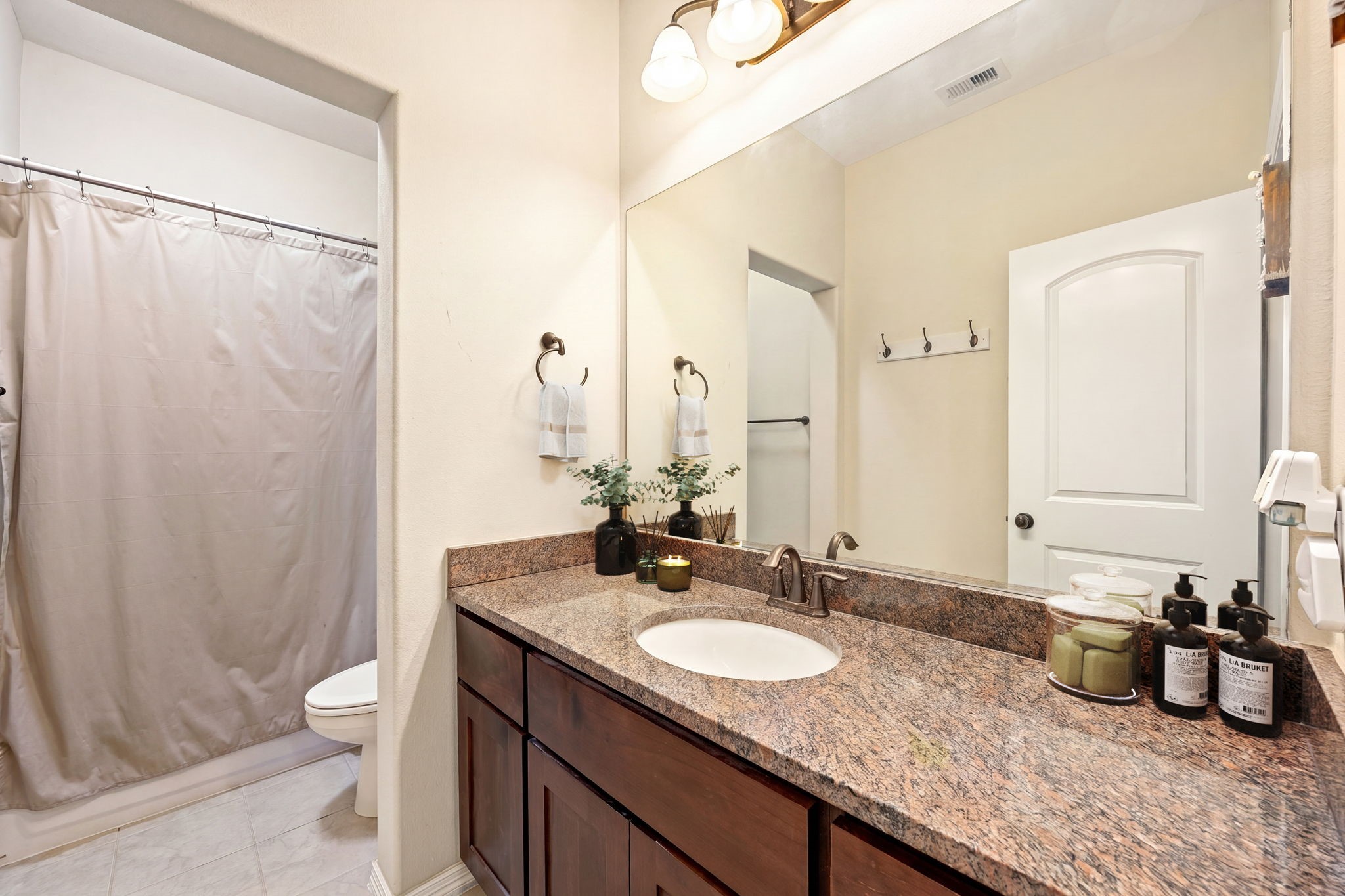 Secondary bath with granite countertops, dark wood cabinetry, a large vanity mirror, tub/shower combo, and tile flooring, clean, functional, and ready for move-in!