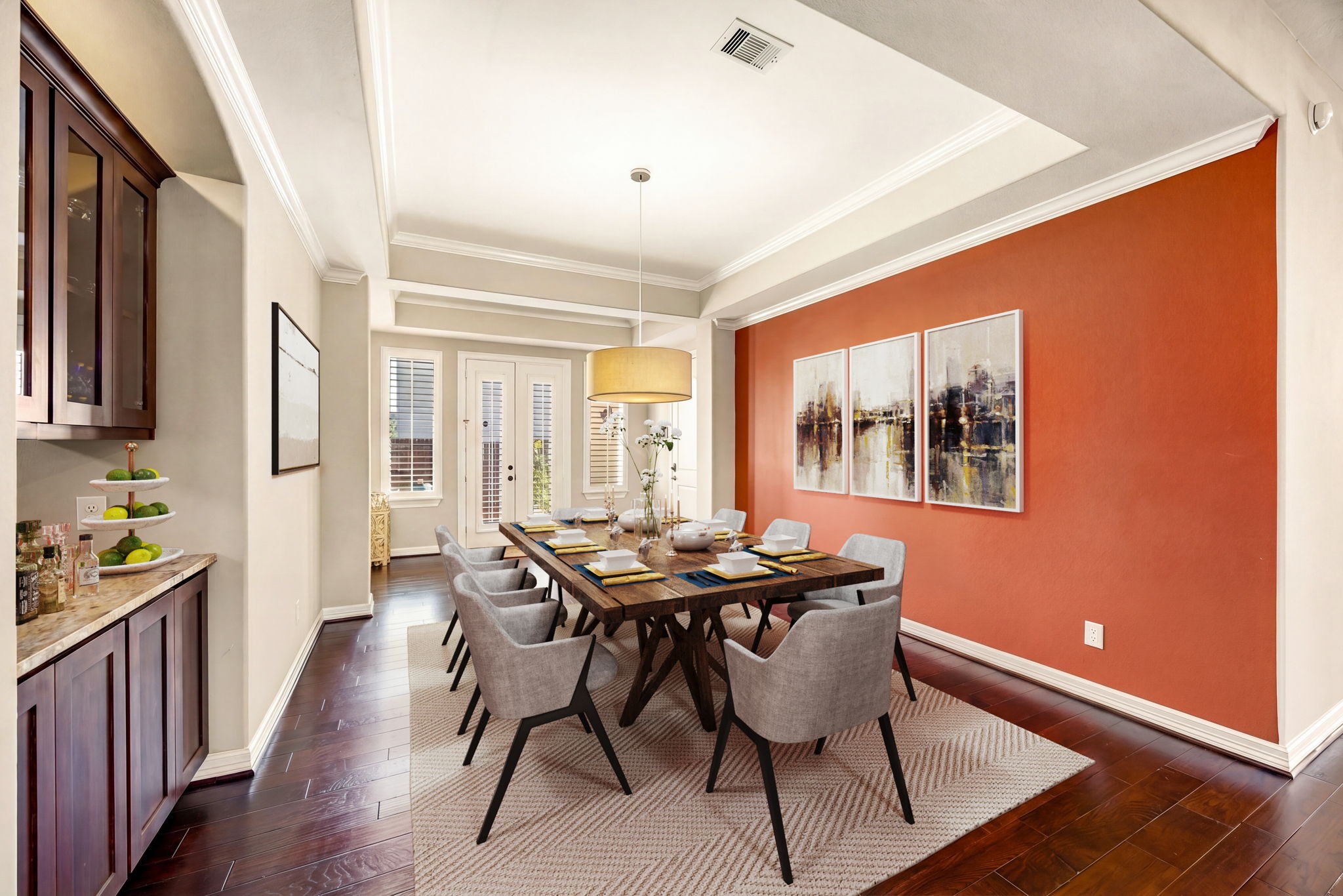 Formal dining made fabulous! This spacious dining room features a bold terracotta accent wall, tray ceiling with crown molding, rich hardwood floors, and a stunning oversized pendant light. French doors with plantation shutters and a built-in wet bar make this the ultimate space for entertaining. *Virtually Staged Formal dining made fabulous! This spacious dining room features a bold terracotta accent wall, tray ceiling with crown molding, rich hardwood floors, and a stunning oversized pendant light. French doors with plantation shutters and a built-in wet bar make this the ultimate space for entertaining. *Virtually Staged