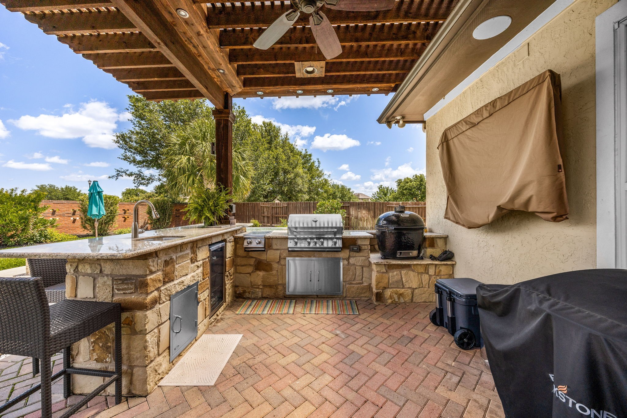 Grill masters, this one's for you! This incredible outdoor kitchen features a stacked stone surround, built-in grill, granite countertops, sink, and a gorgeous wood pergola with ceiling fan overhead. Entertaining just reached a whole new level!