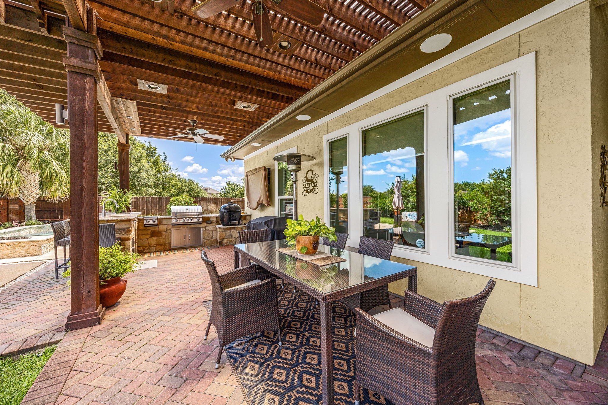 Al fresco living at its finest! This expansive covered patio features a stunning wood pergola, recessed lighting, ceiling fans, brick pavers, and a direct view of the outdoor kitchen and pool, the perfect outdoor escape!