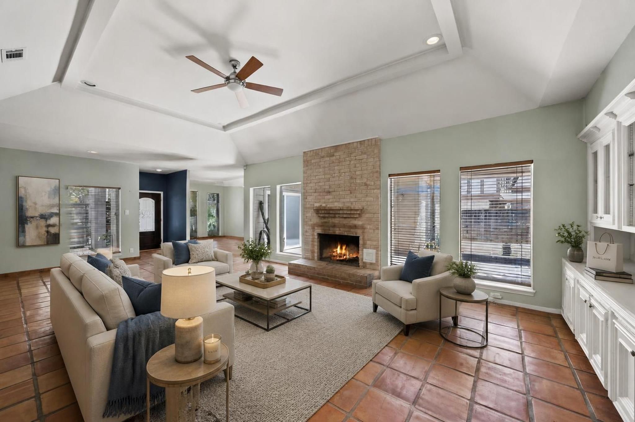 The living room opens into a dramatic main gathering space with vaulted ceilings, tile flooring, a gaslog fireplace, and wide views toward the backyard. The scale of the room creates a strong central point for the home. Virtually staged.