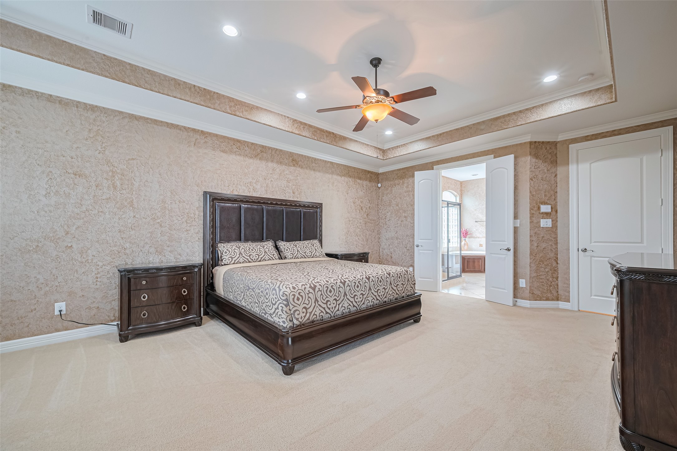 Another view of the spacious primary suite showcasing the elegant tray ceiling, generous layout, and direct access to the en-suite bathroom.
