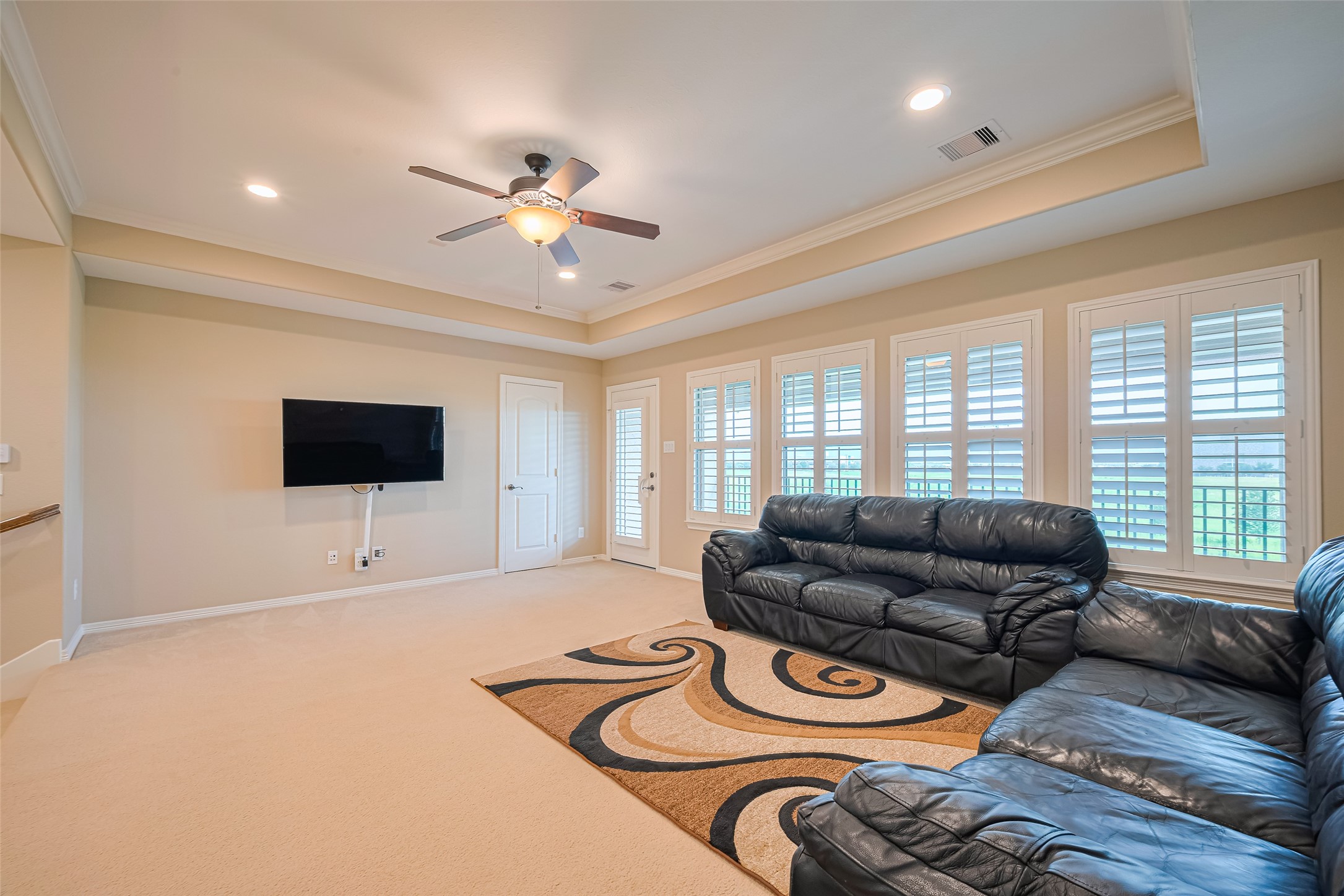 Spacious upstairs game room framed by plantation shutters, a tray ceiling, and direct access to the private balcony.