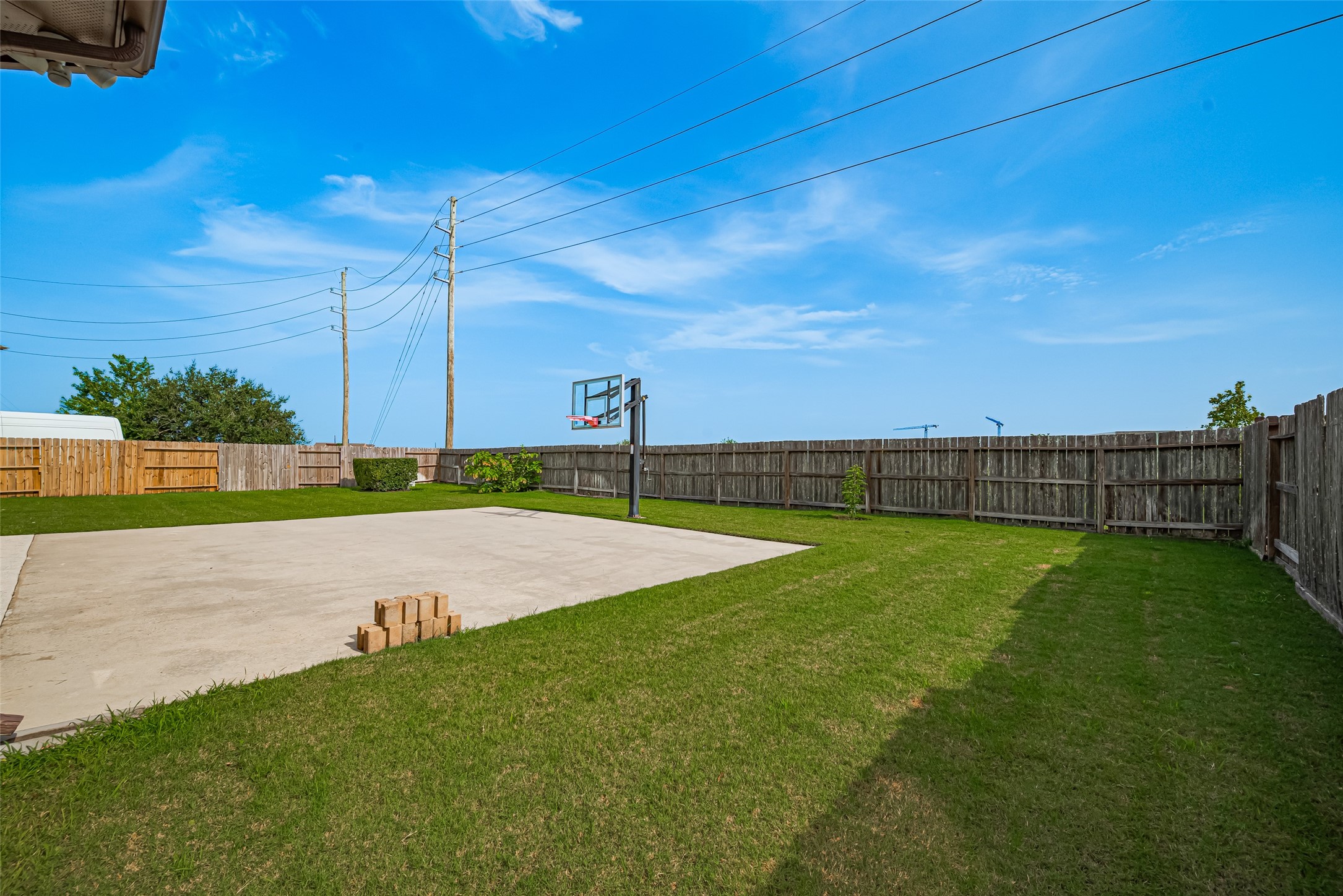 Expansive fenced backyard featuring a large concrete basketball court and generous green space, offering plenty of room for recreation and outdoor activities.