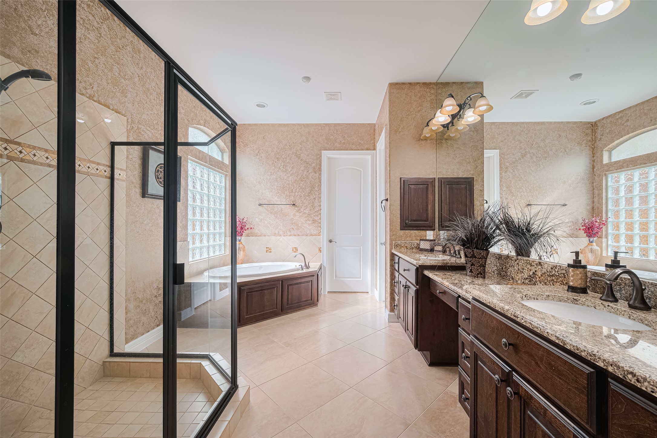 Luxurious primary bathroom featuring a glass-enclosed walk-in shower, relaxing soaking tub, extended granite vanity, and generous cabinetry.
