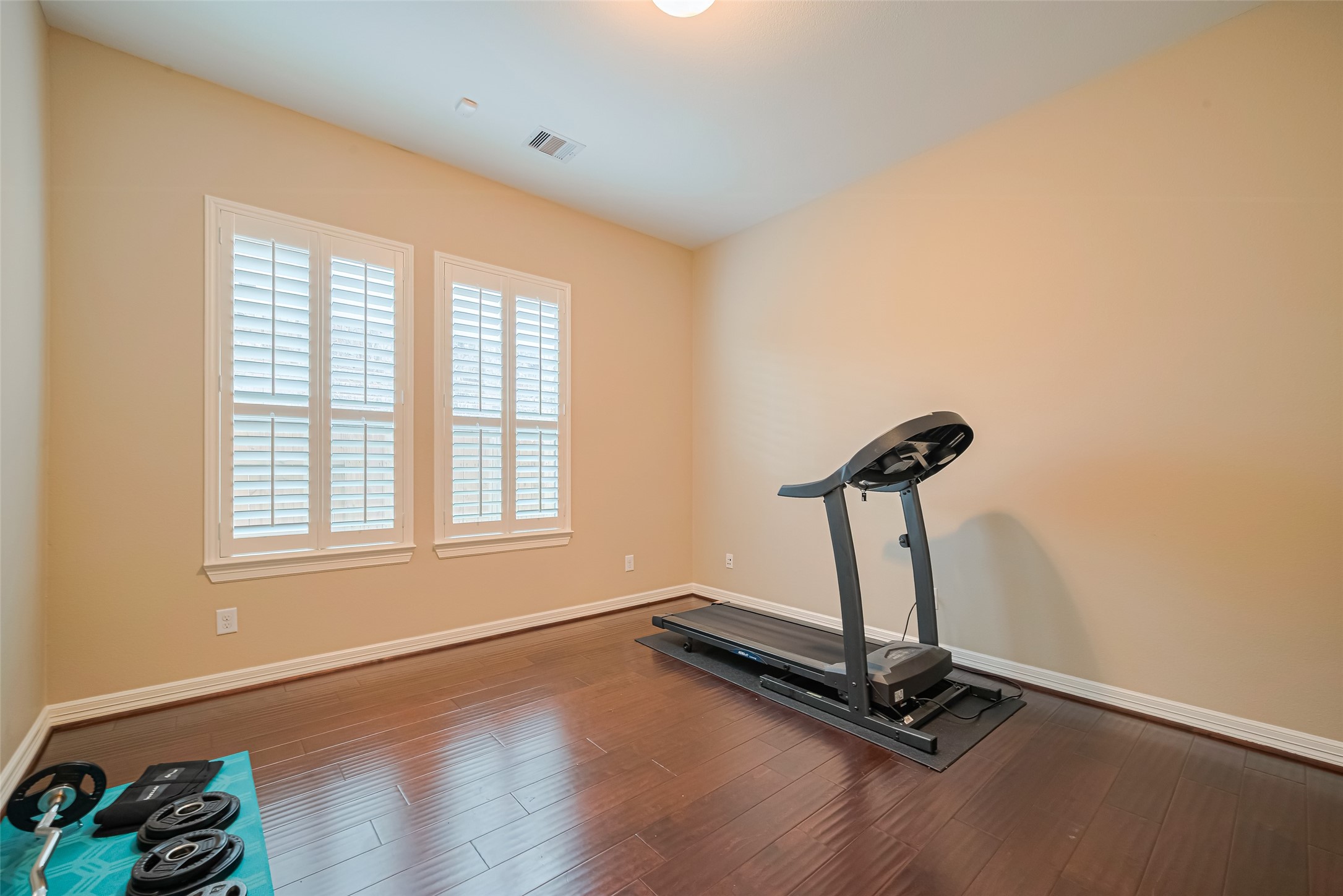 Versatile fitness room with hardwood flooring and plantation-shuttered windows, offering ample space for a personalized home gym.