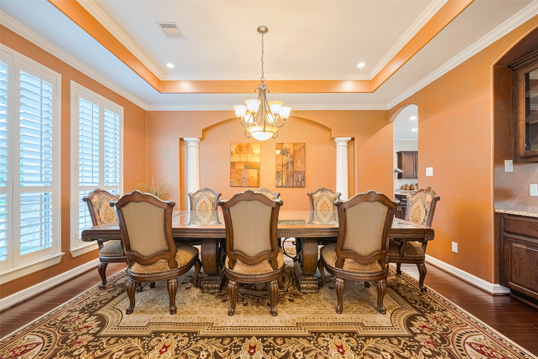 Formal dining room appointed with rich hardwood floors, plantation shutters, a tray ceiling, and an elegant chandelier.