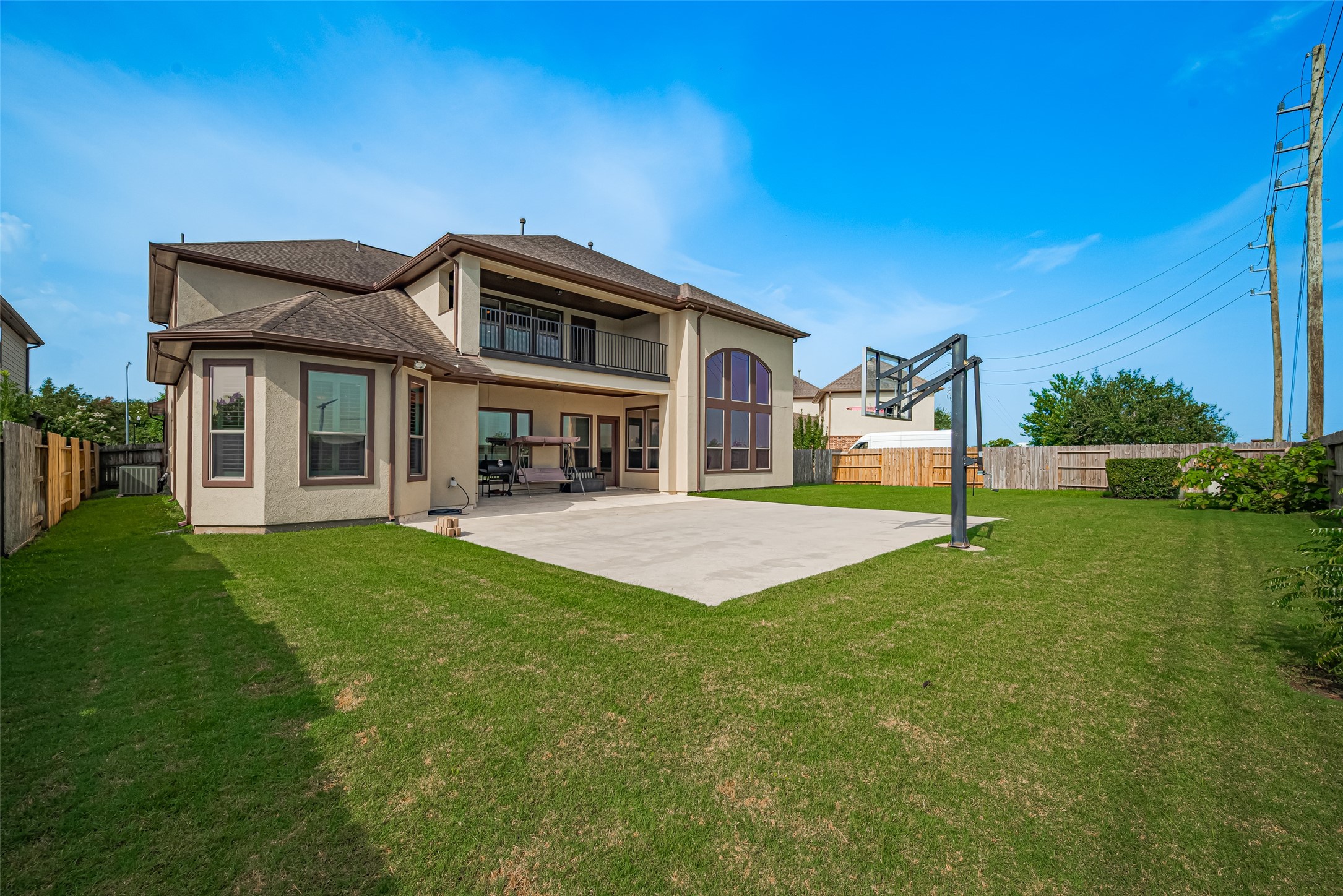 Expansive backyard showcasing the homes impressive rear elevation, covered patio and upper balcony, complemented by a large basketball court and generous lawn space.