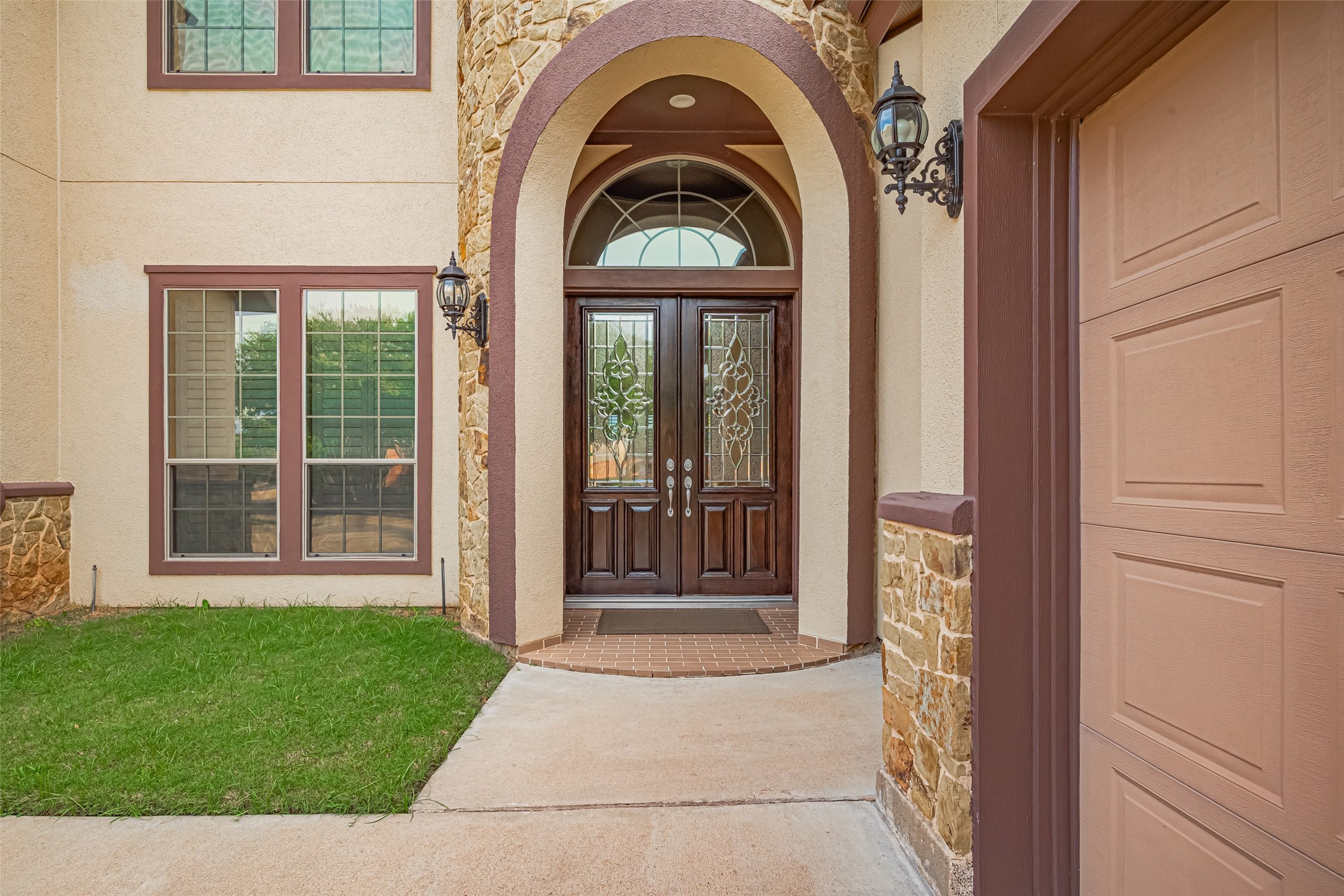 Welcoming covered entrance framed by stonework, decorative double doors, and a graceful arched transom.