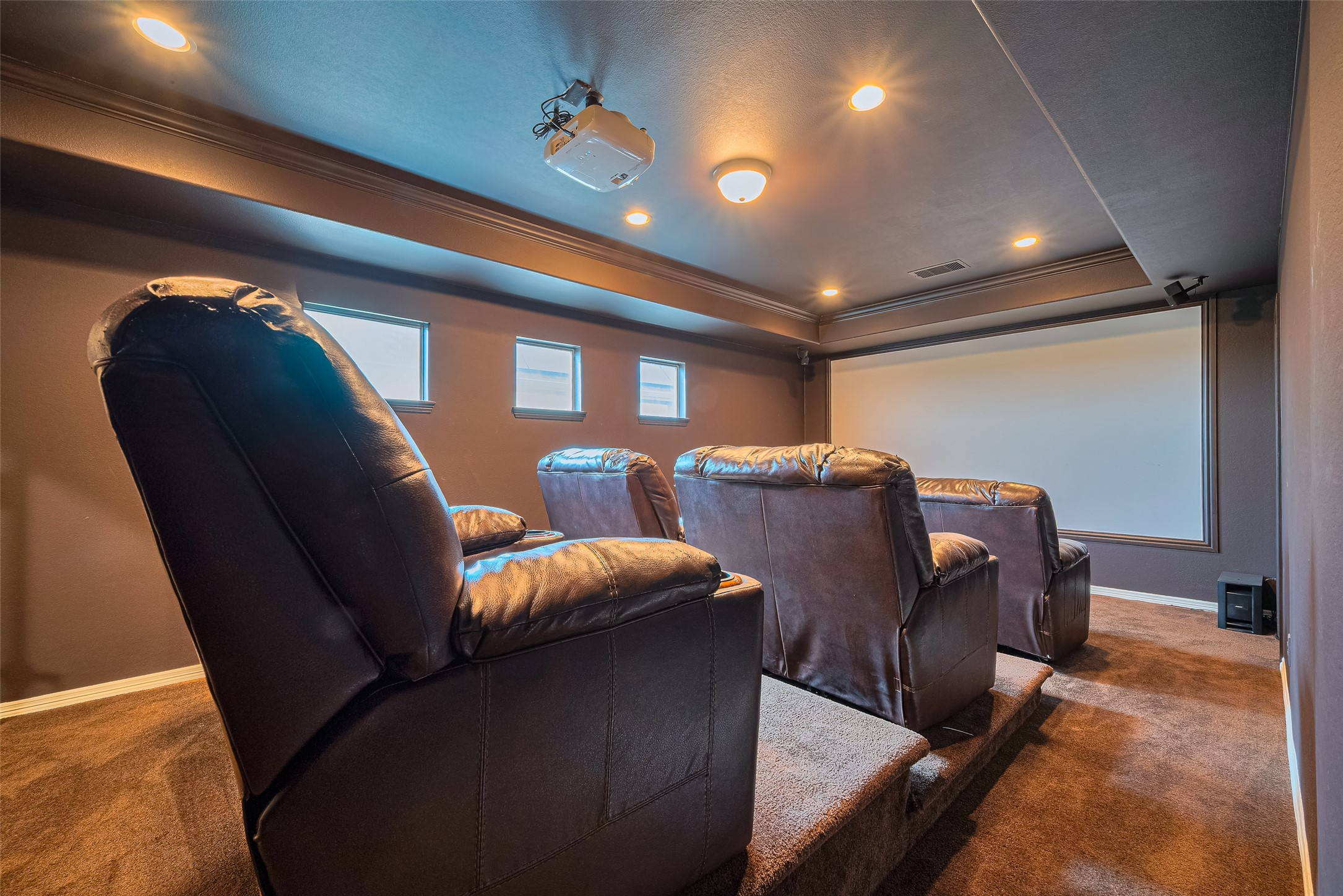 Dedicated home theater featuring tiered leather seating, a large projection screen, ceiling-mounted projector, and immersive surround sound.