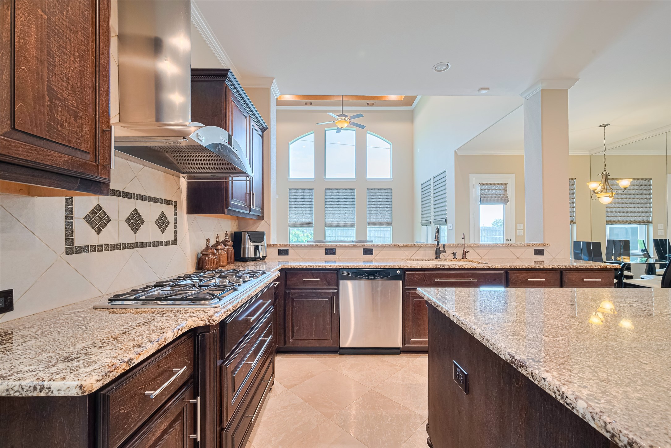 Opposite kitchen perspective capturing the decorative tile backsplash, integrated dishwasher, expansive prep surfaces, and clear views toward the breakfast and family areas.