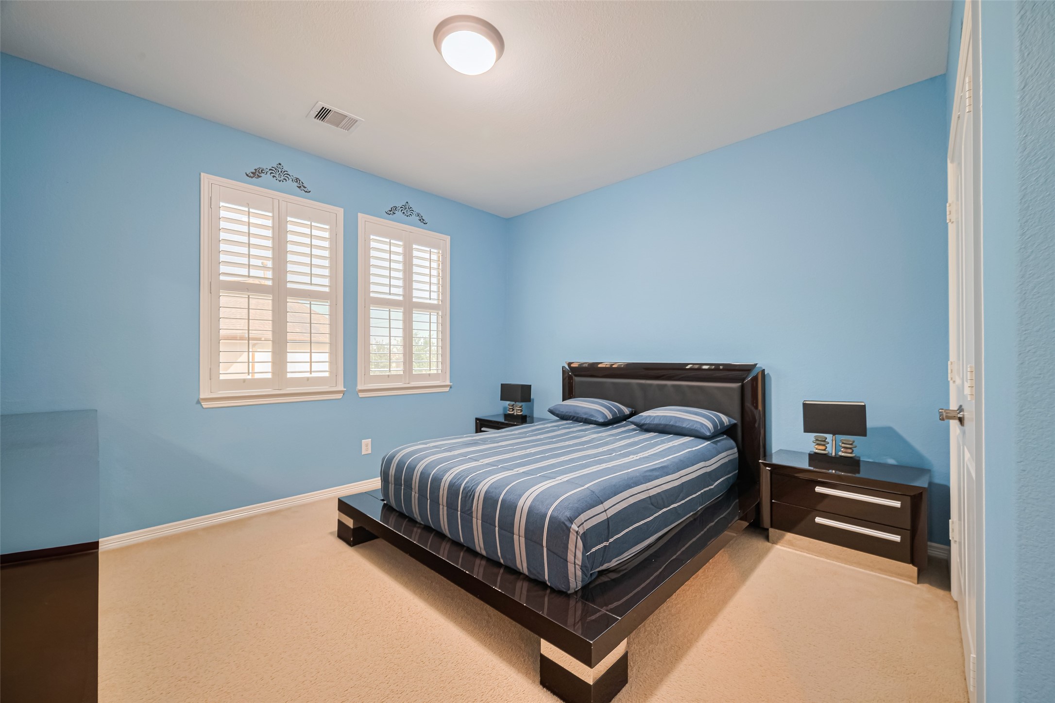 Spacious secondary bedroom featuring calming blue tones, plush carpeting, generous natural light, and ample room for comfortable furnishings.