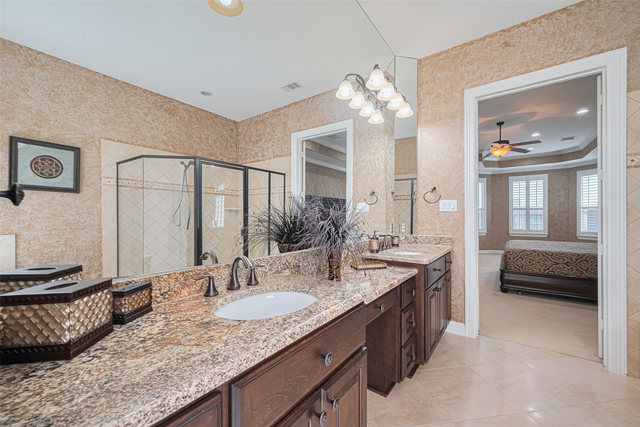 Elegant primary bathroom showcasing dual granite vanities, expansive mirrors, rich cabinetry, and a spacious walk-in shower.