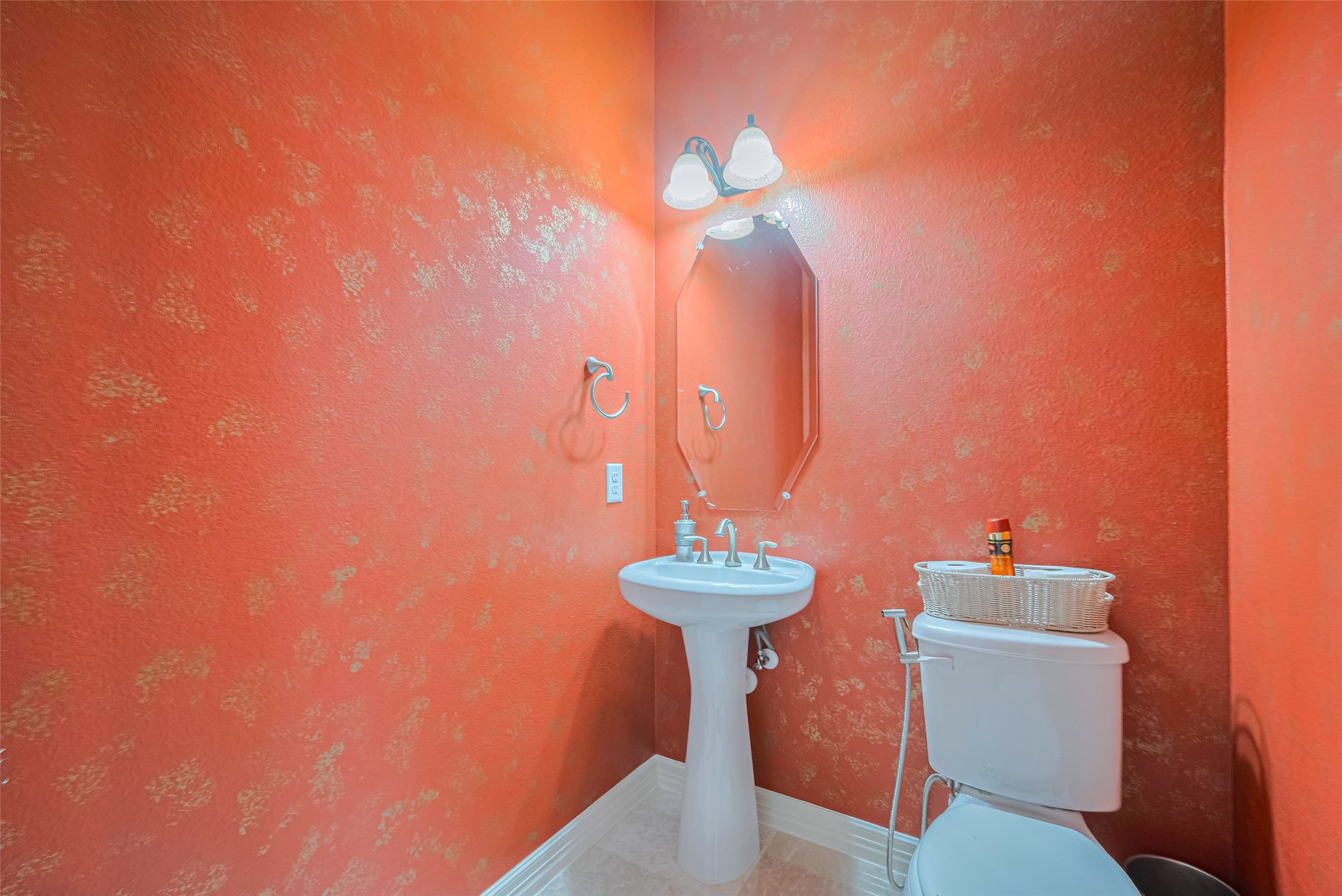 Stylish powder room featuring a pedestal sink, geometric mirror, and warm textured accent walls.